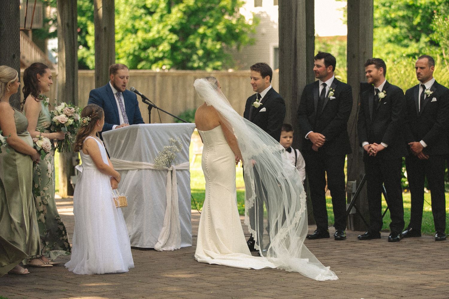 Wedding ceremony taking place under an elegant outdoor pavilion with white decor.