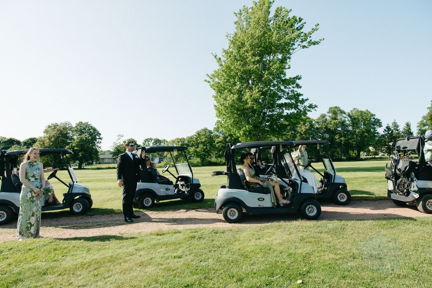 Golf carts parked on grass with wedding party gathering nearby.
