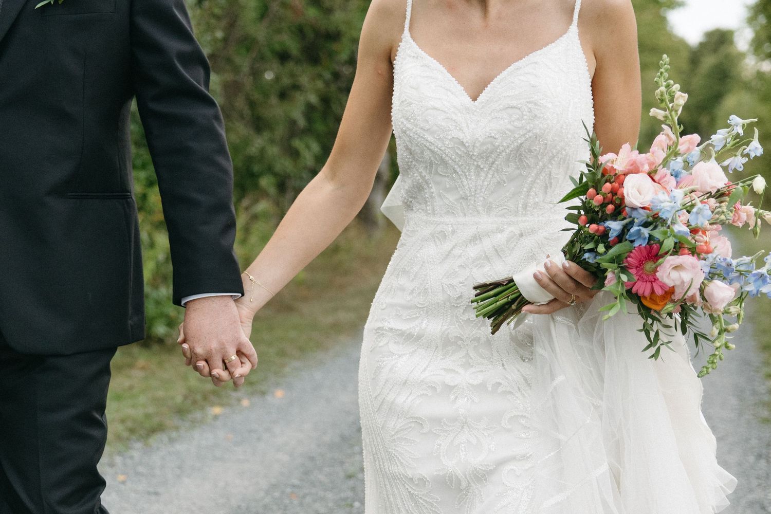Close-up view of a white lace wedding dress and colorful floral bouquet in an outdoor setting.