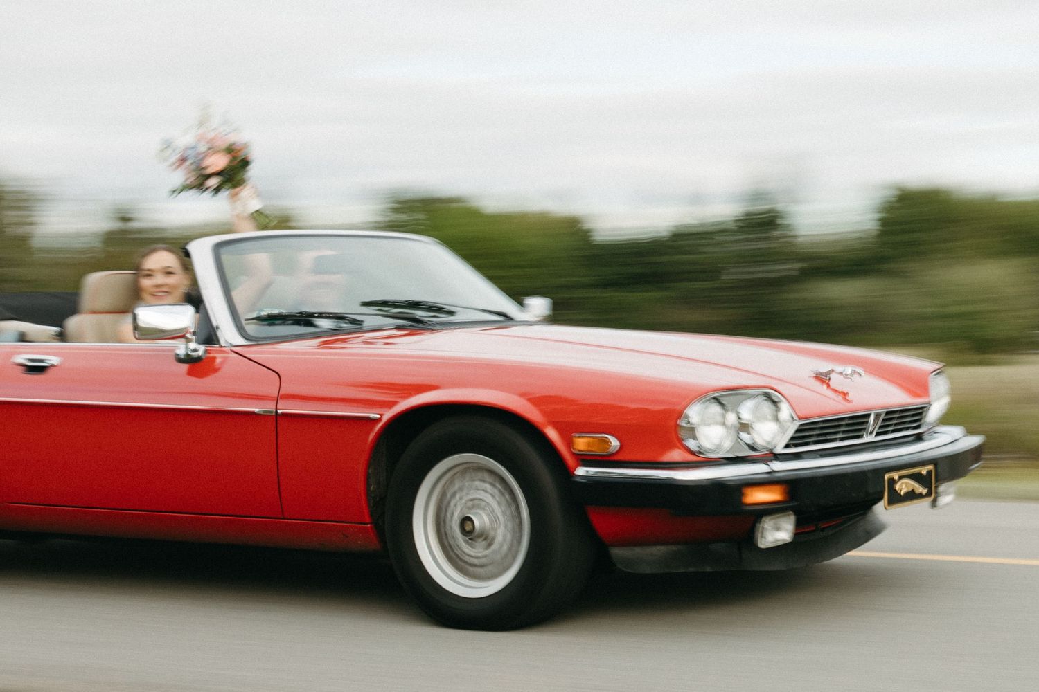 Red vintage convertible car in motion on a country road.