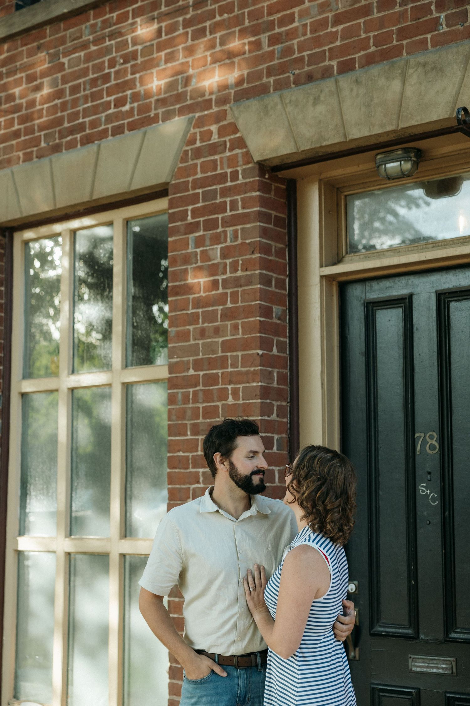 A couple shares an intimate moment outside a historic brick building with black shutters.