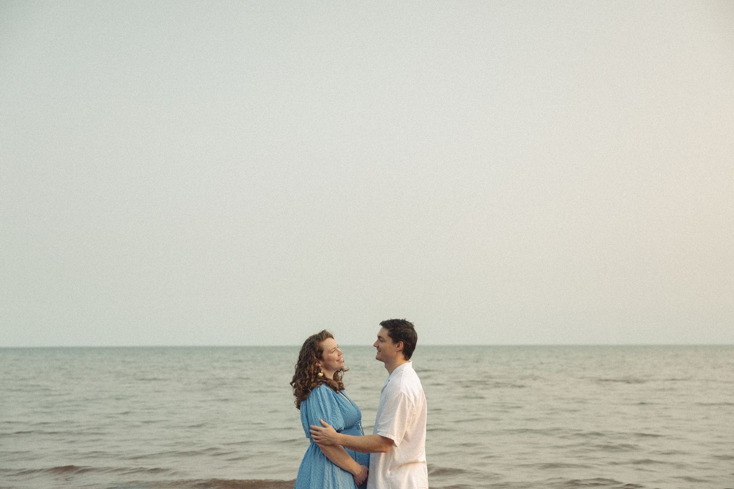 A couple shares an intimate moment by the ocean during golden hour.