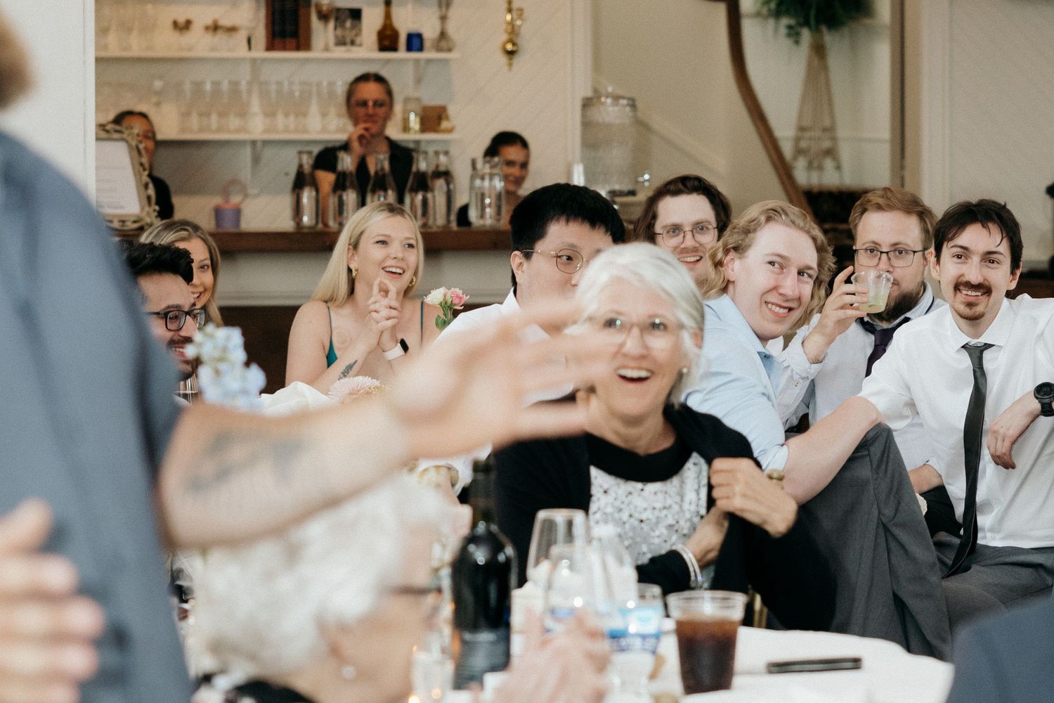 Wedding guests laugh and react emotionally during speeches at an elegant indoor reception.