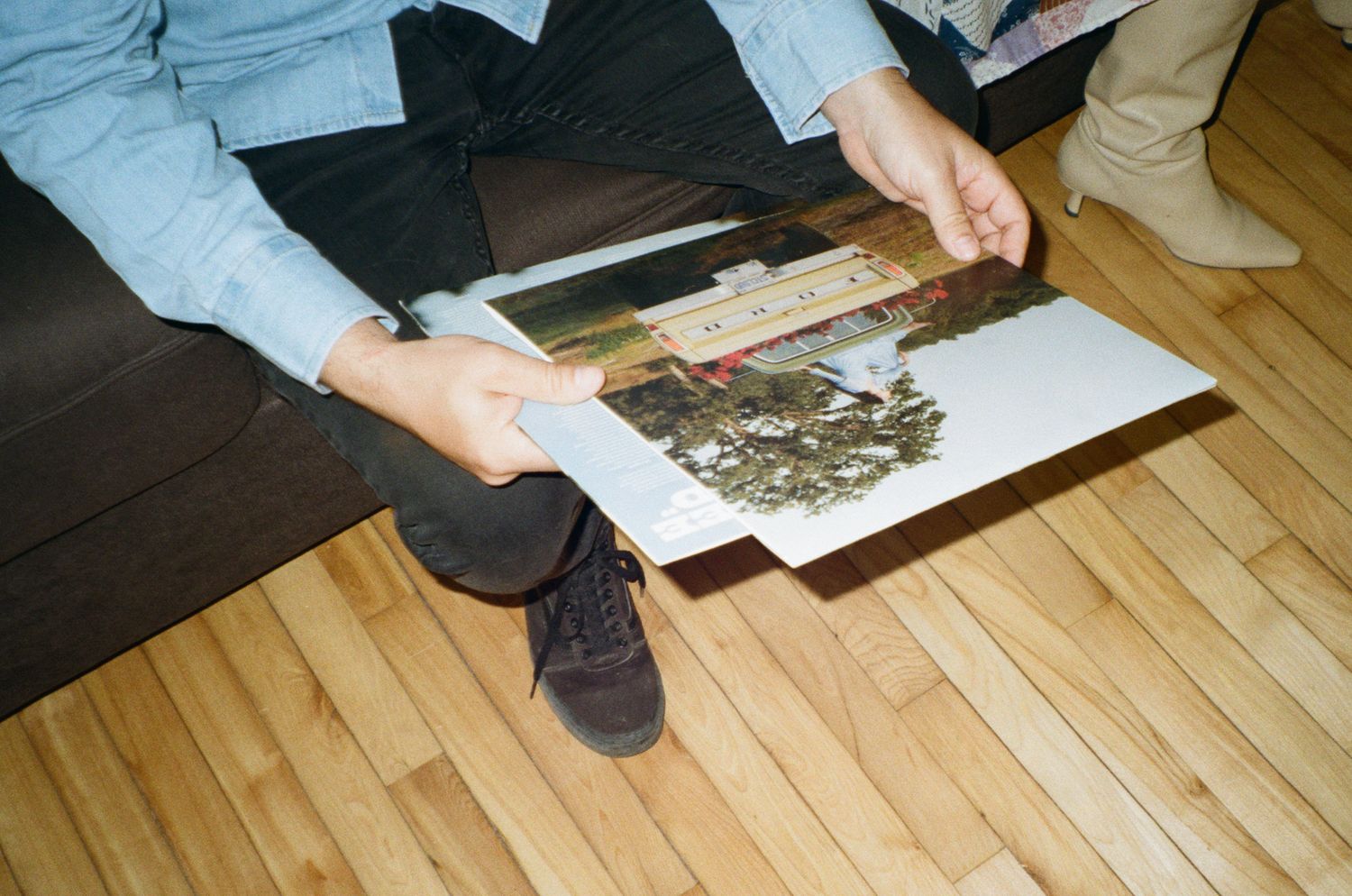 Person sitting on floor holding a large botanical print with pressed plants and foliage on wooden flooring.