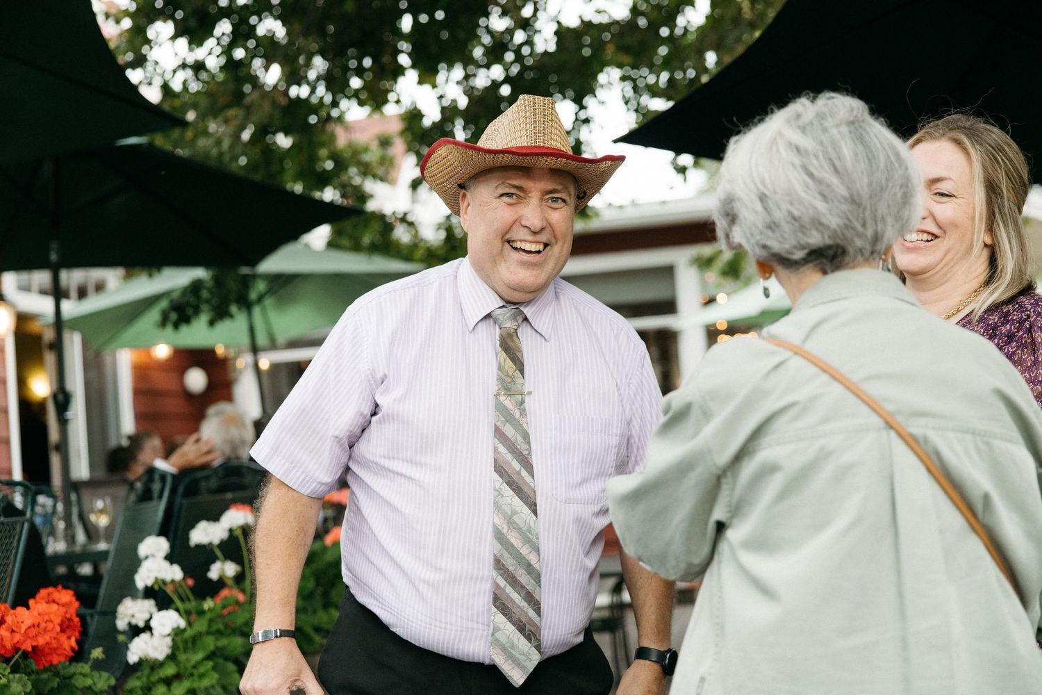 Smiling man in cowboy hat and tie greeting guests at an outdoor wedding reception.