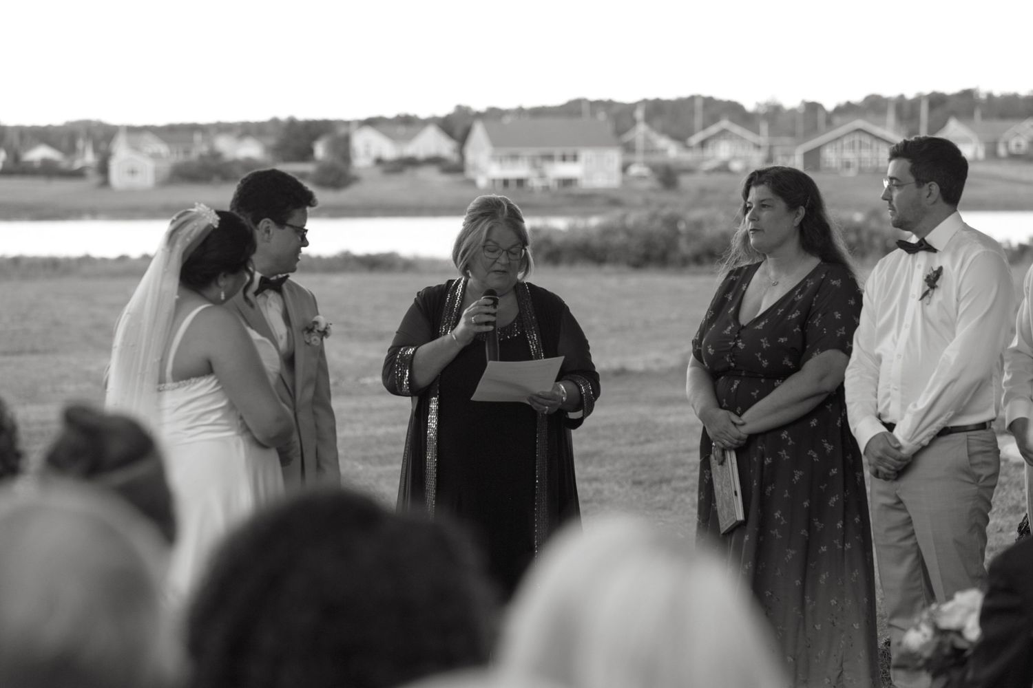 Black and white photo of wedding ceremony with officiant reading vows as bride, groom and guests look on.