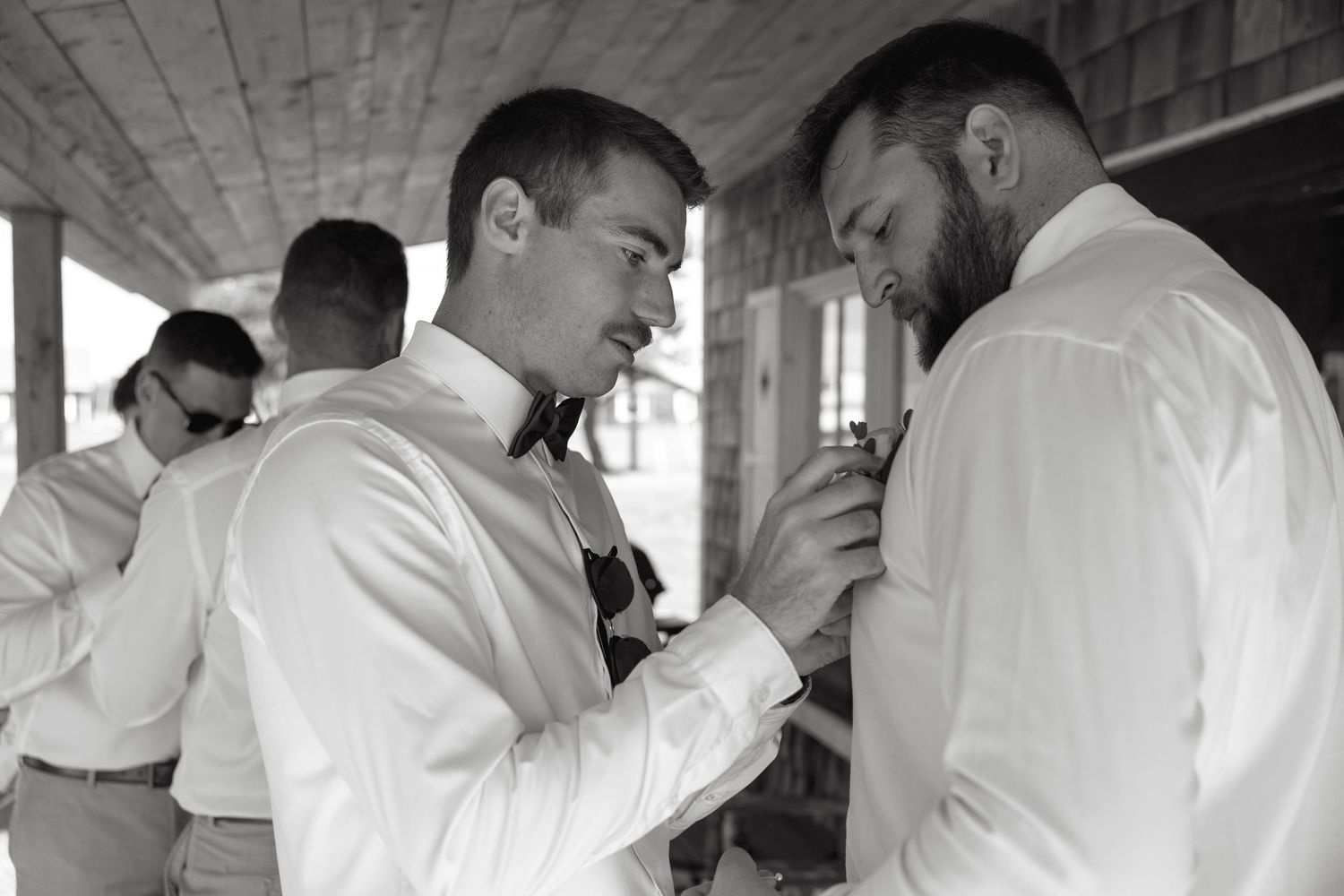 Black and white photo of groomsmen helping each other with bow ties while getting ready for a wedding ceremony.