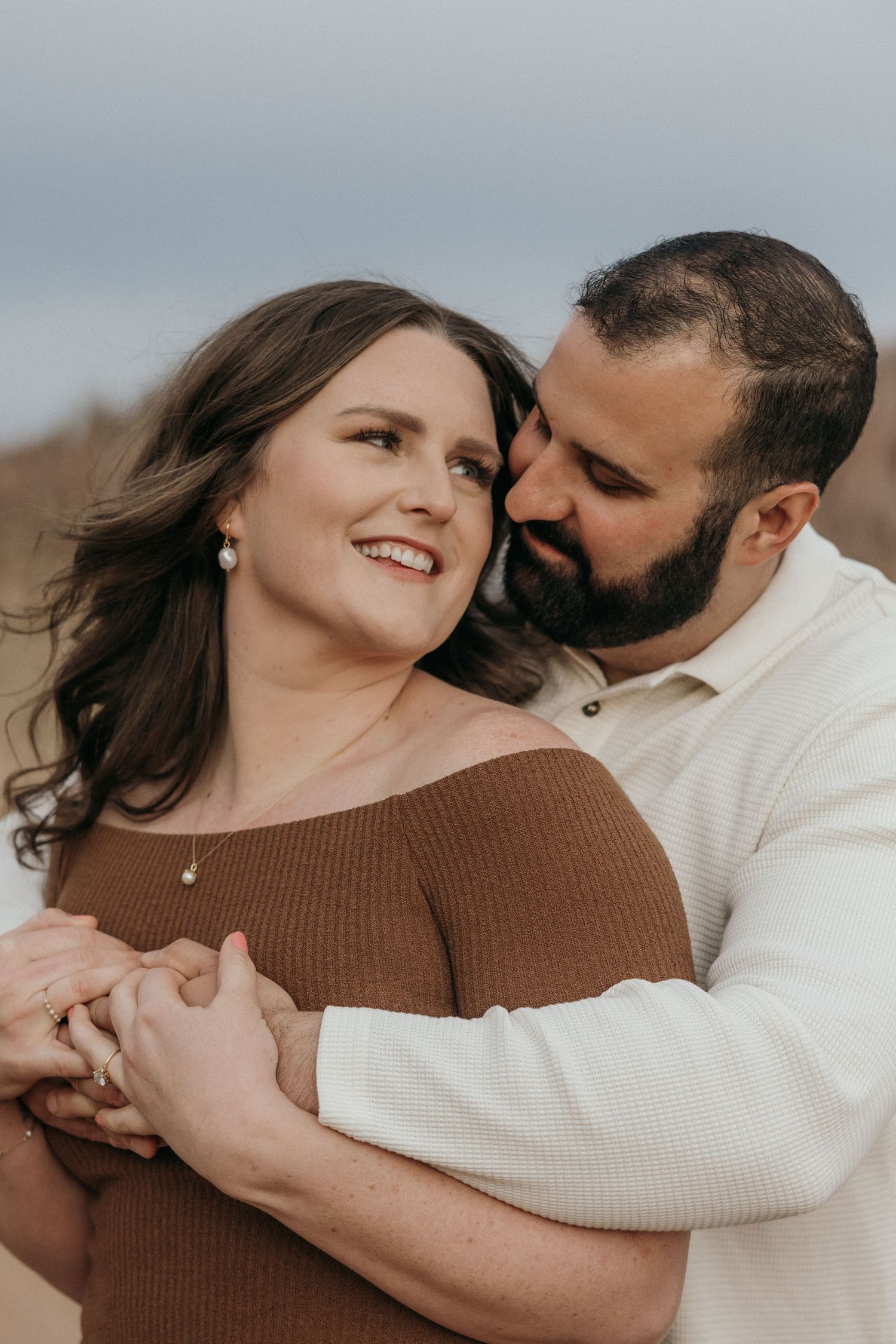 A romantic couple in brown and white sweaters embrace tenderly in a series of intimate outdoor portrait photos.