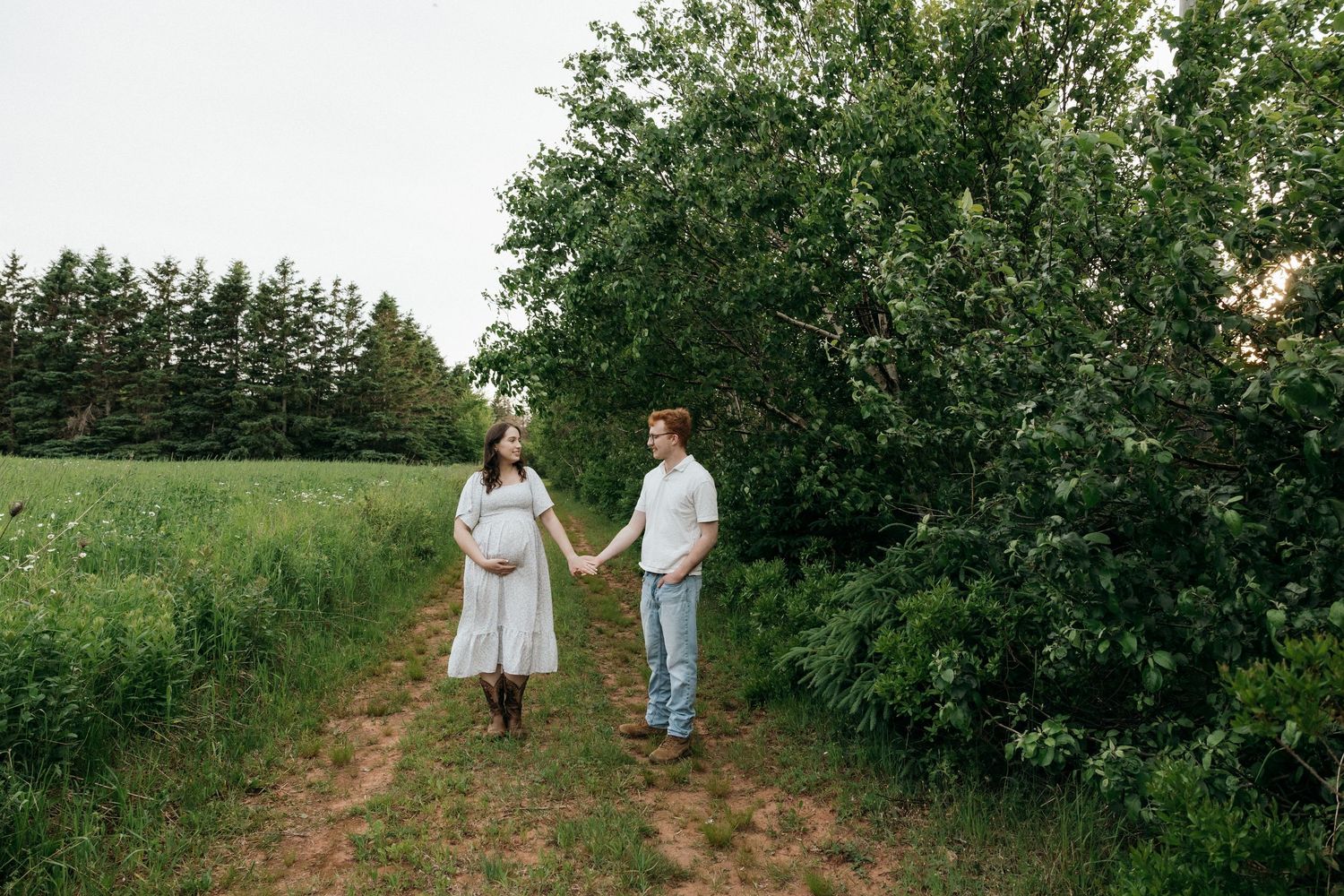 Couple walking together on a dirt path surrounded by lush greenery and trees.