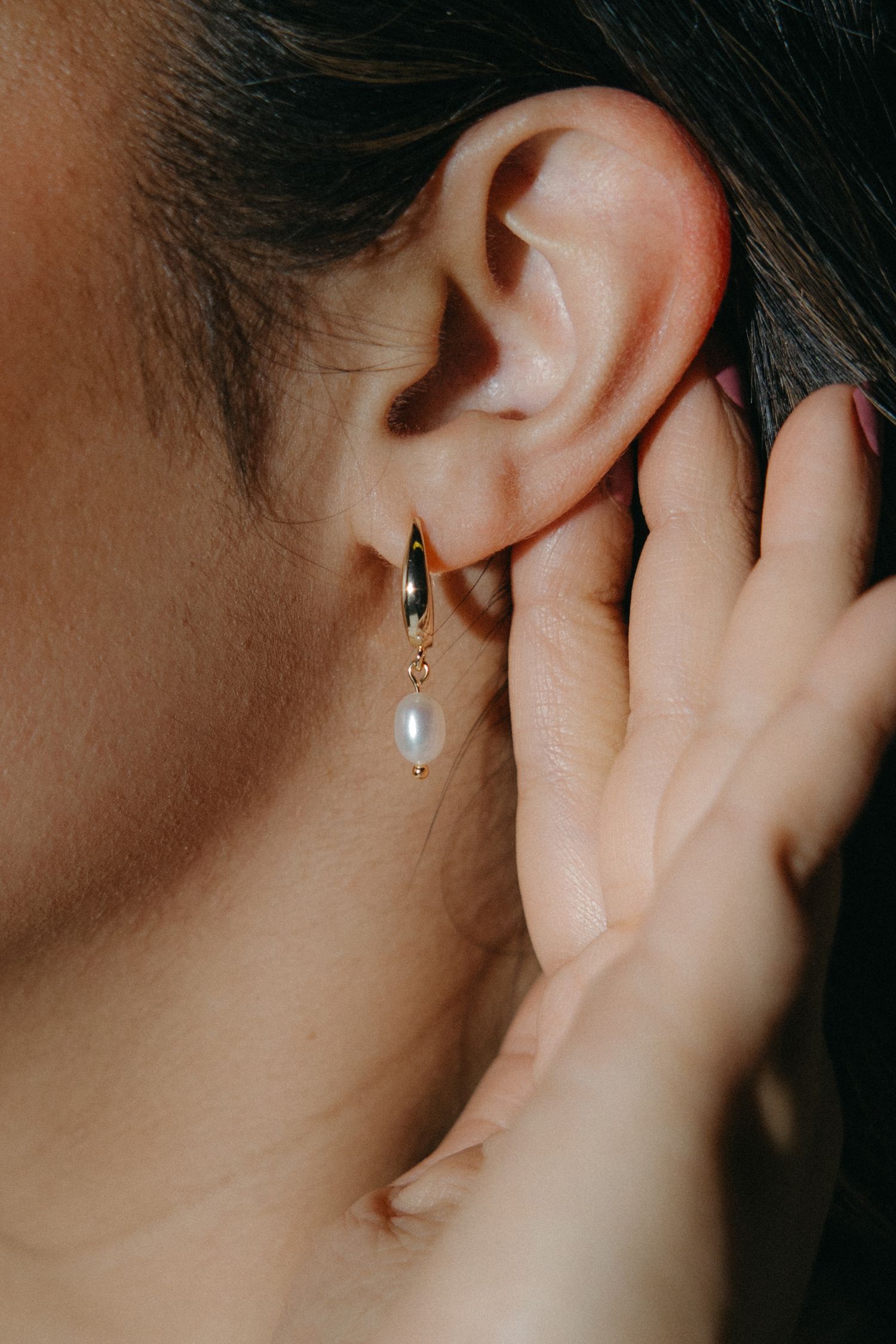 Close-up view of a pearl drop earring being worn, showing multiple angles of the delicate jewelry piece.