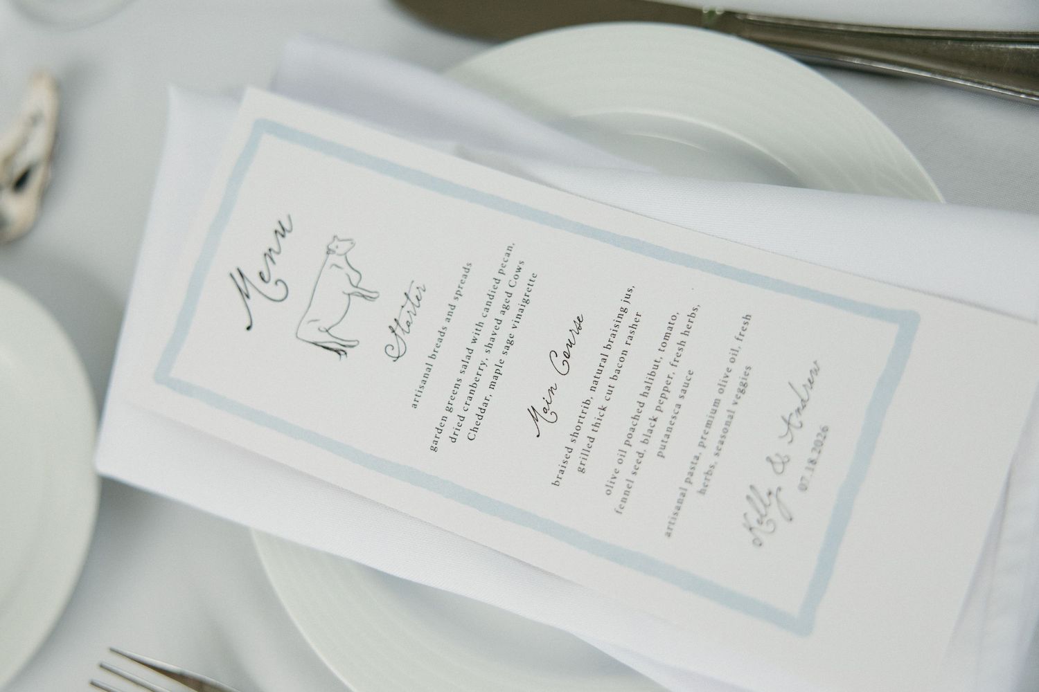 Elegant wedding menu card with blue border on a white tablecloth with silverware.
