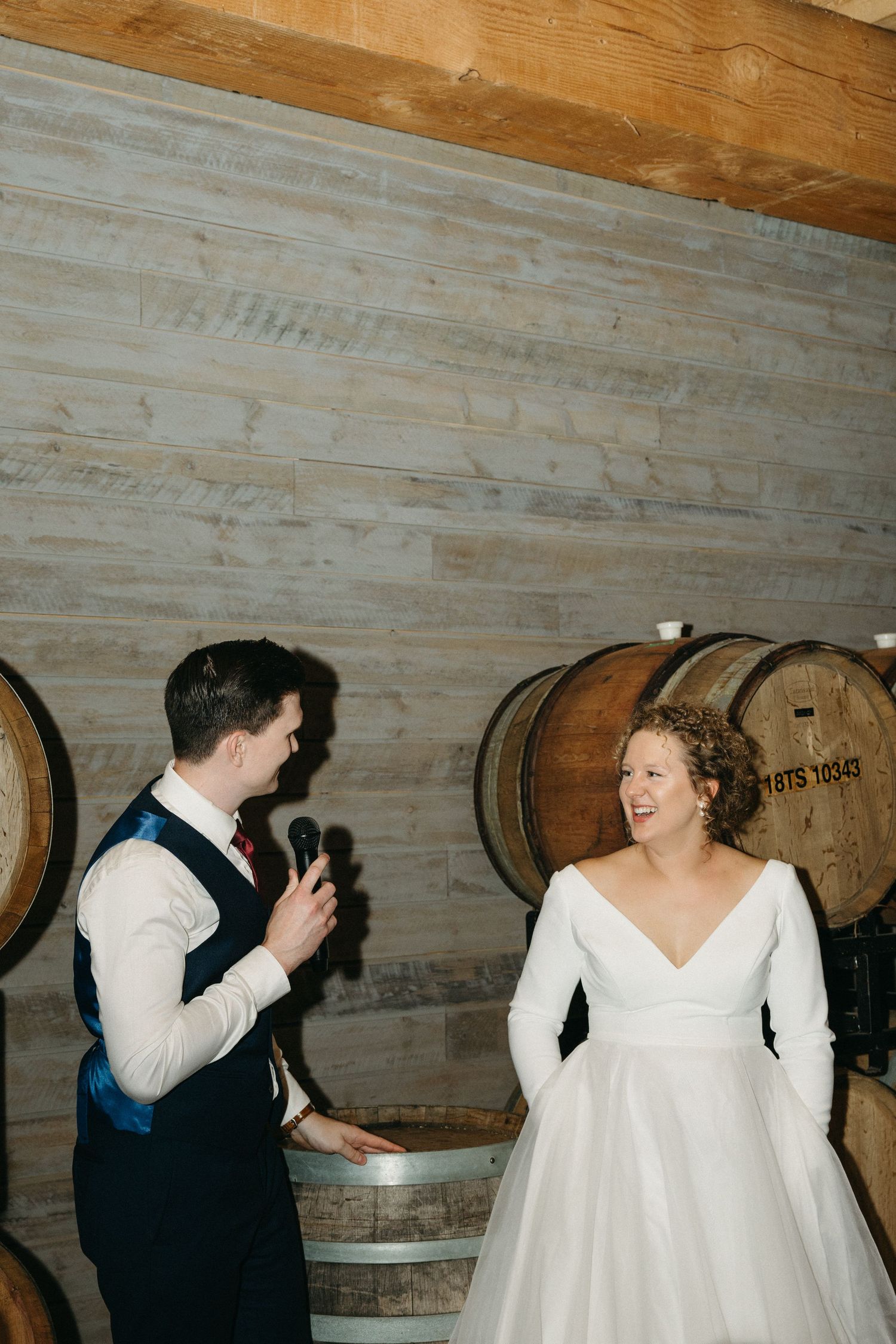 Wedding couple poses near wooden barrel wall during reception.