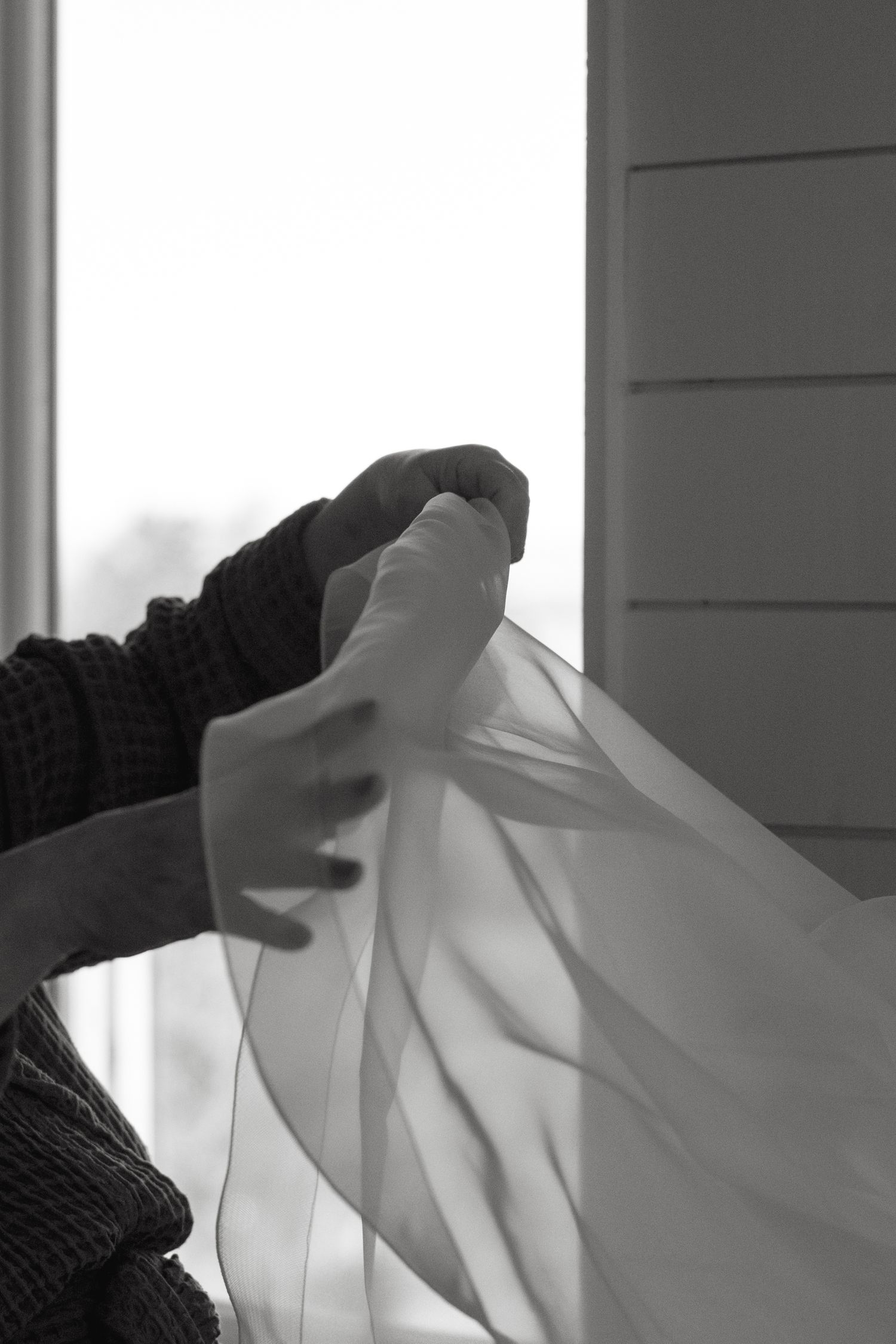 Hands adjusting white fabric in close-up black and white photography.