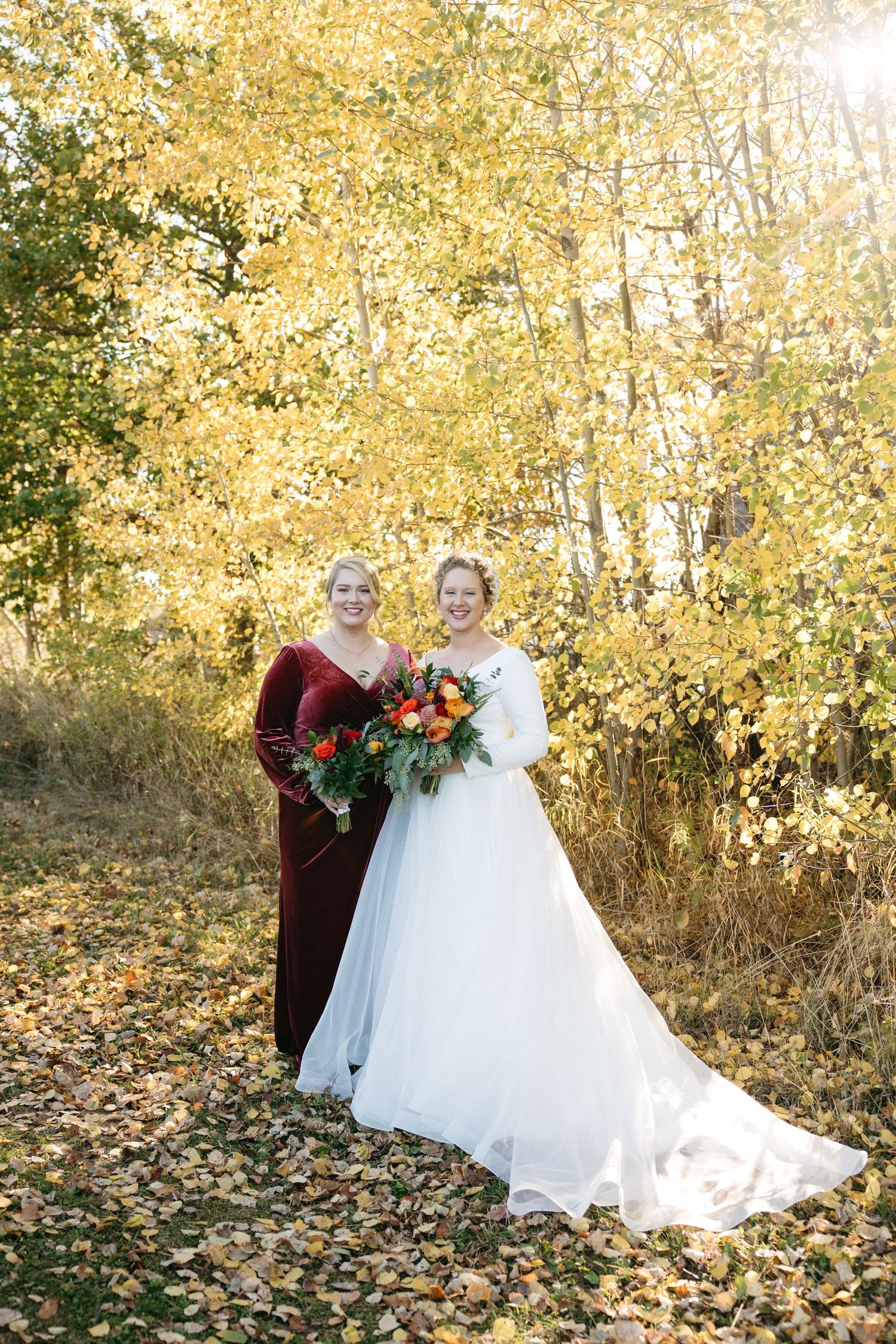 Wedding portrait with burgundy and white attire against vibrant fall foliage.