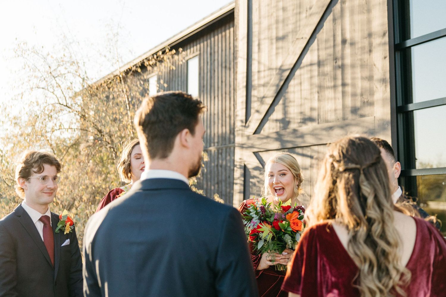 Wedding party members gather outside a modern building during golden hour.