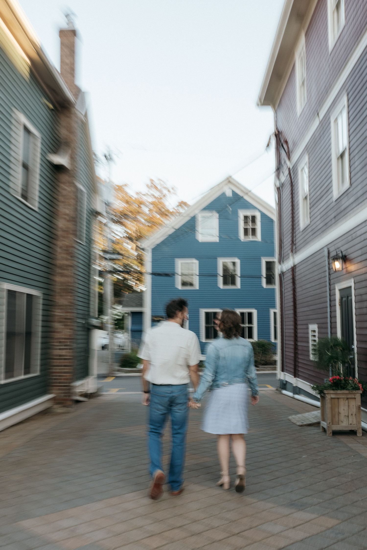 A couple walks between blue residential buildings at dusk.