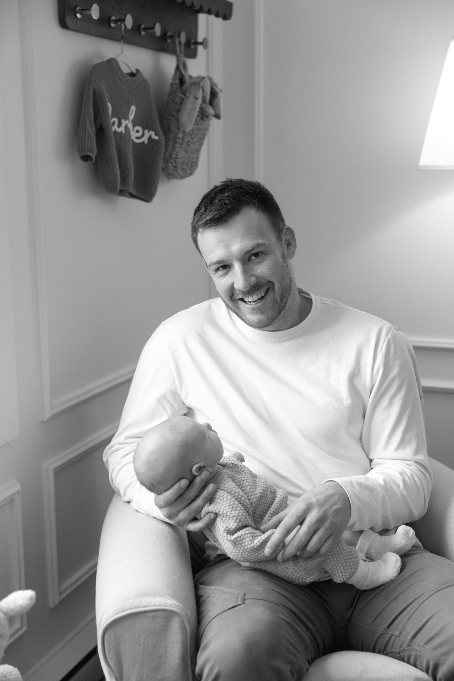 A joyful black and white nursery scene with a wooden wall rack displaying a 'Parker' sweater.
