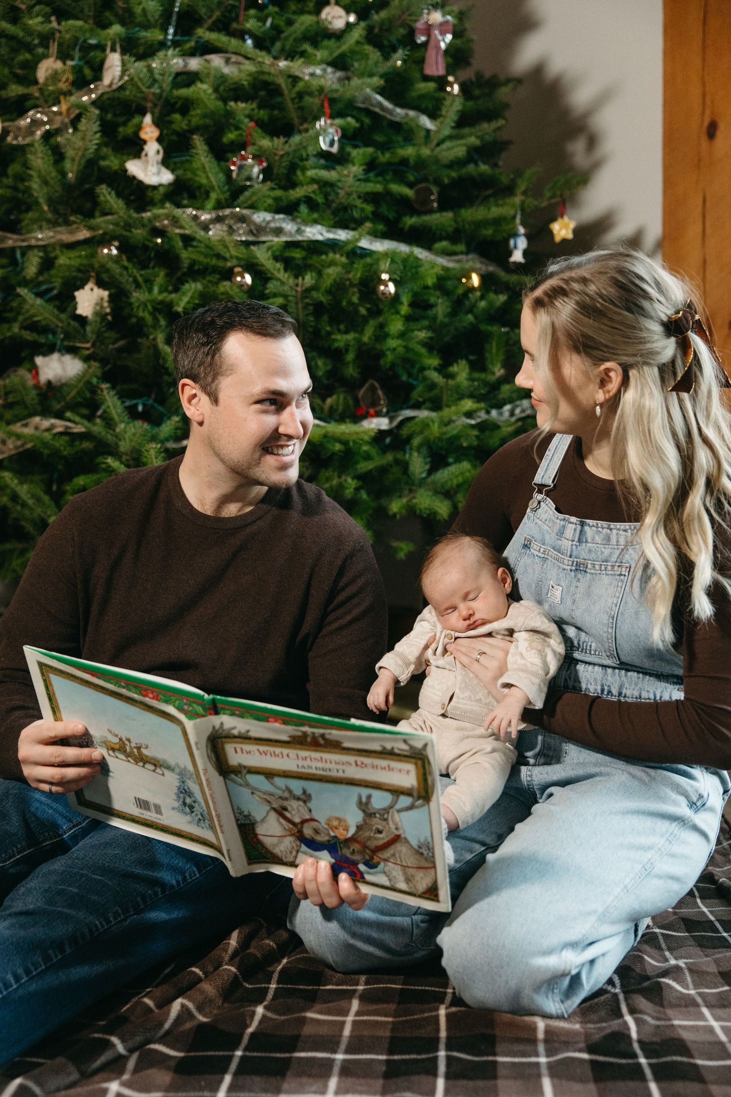 Family sharing tender moments while reading together near a decorated Christmas tree.