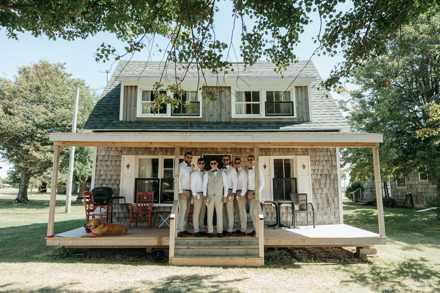 A charming white farmhouse with a wraparound porch decorated for a wedding celebration.