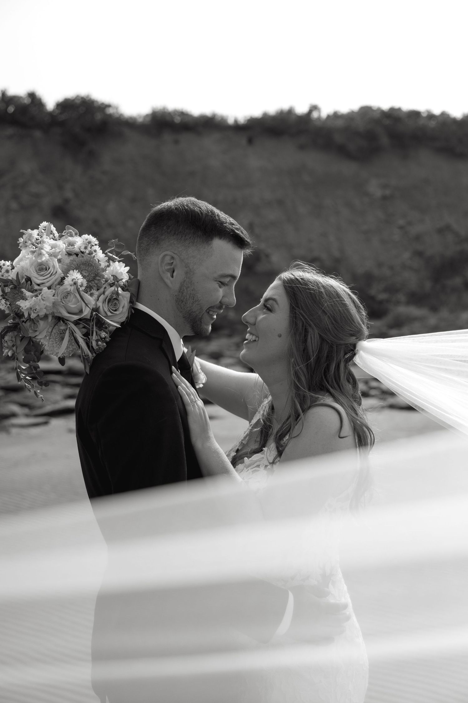 Intimate wedding moment captured through flowing white veil on beach.