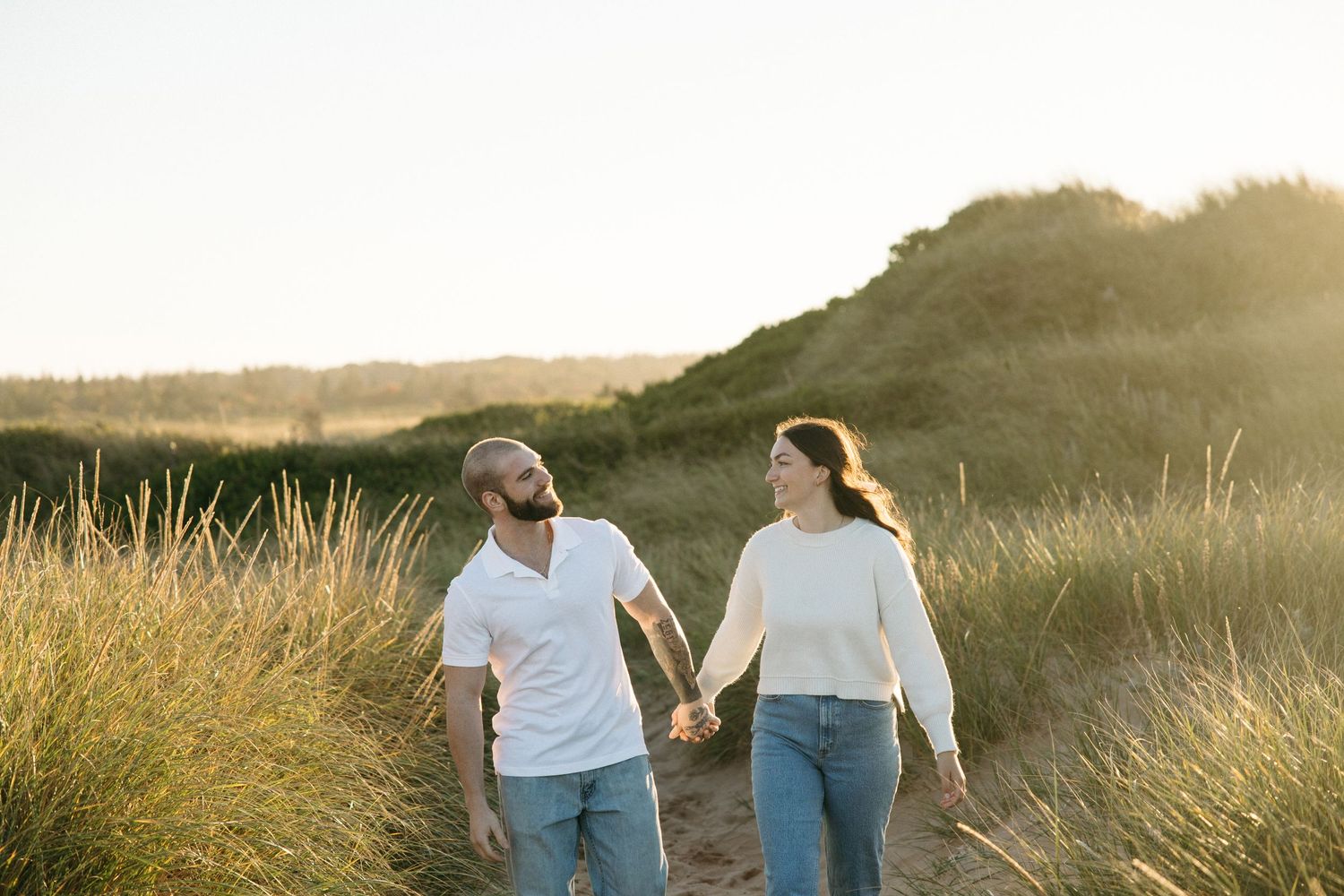Couple walking together through a sunlit field at golden hour.