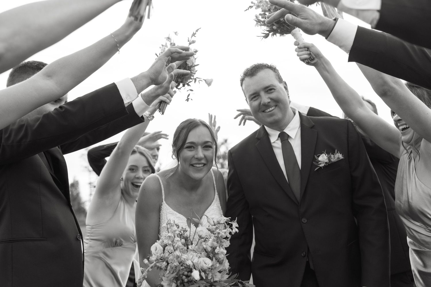 Black and white photo of wedding party members raising their arms to form a tunnel.
