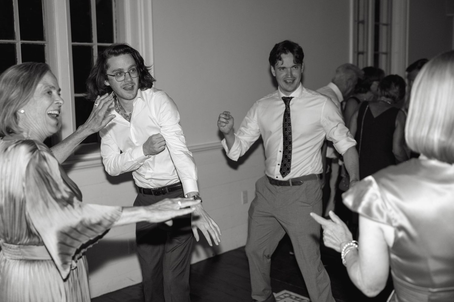 Party guests dancing energetically at a wedding reception in black and white.