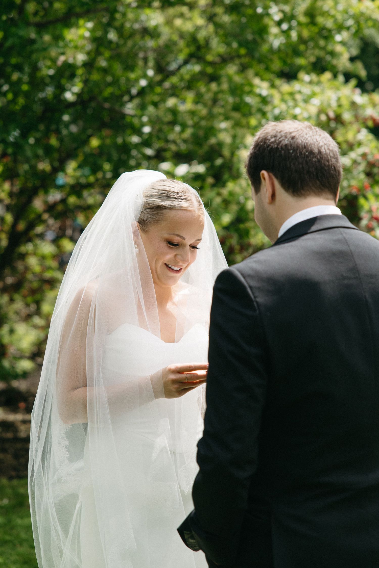 A couple shares a joyful moment outdoors during their wedding ceremony with greenery in the background.