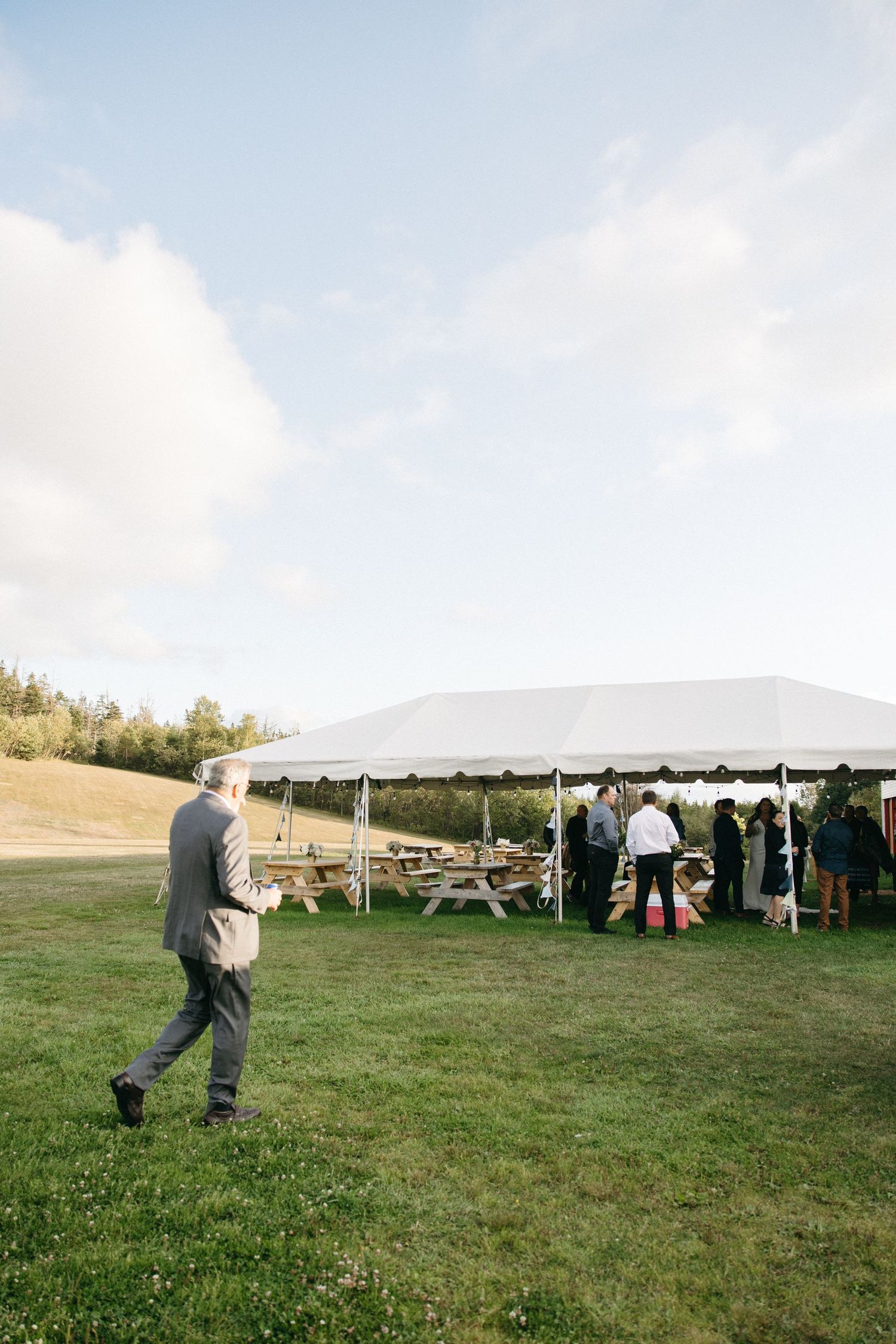 An outdoor event setup with a white tent and picnic tables on a grassy field.