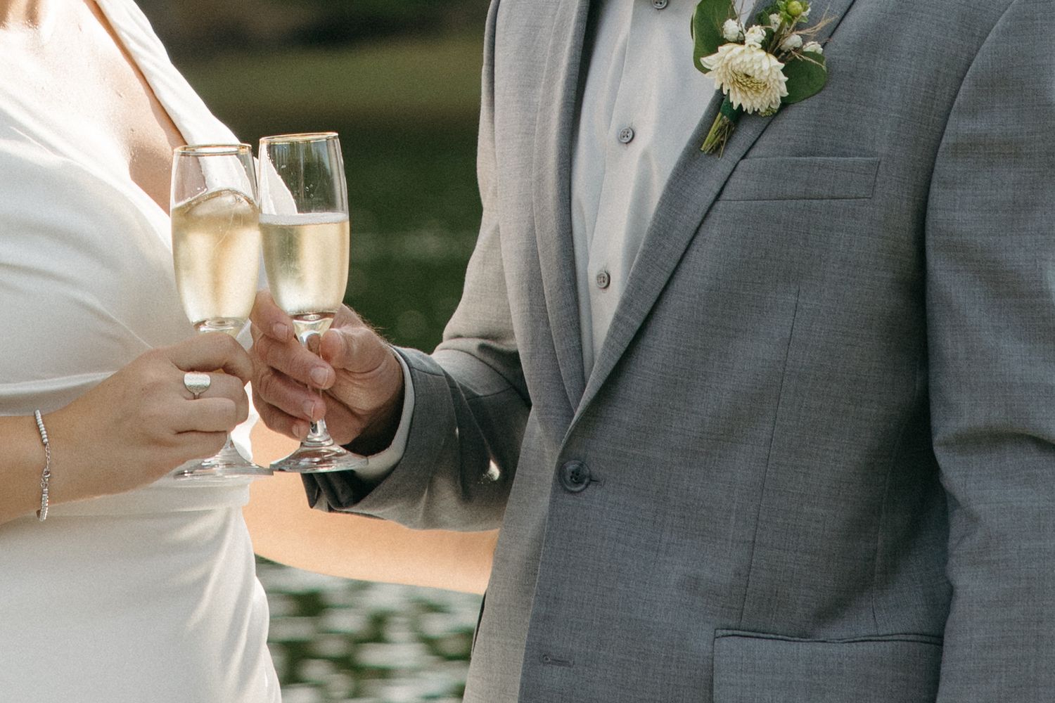 Two people toast champagne glasses while standing on a lakeside dock during a wedding celebration.