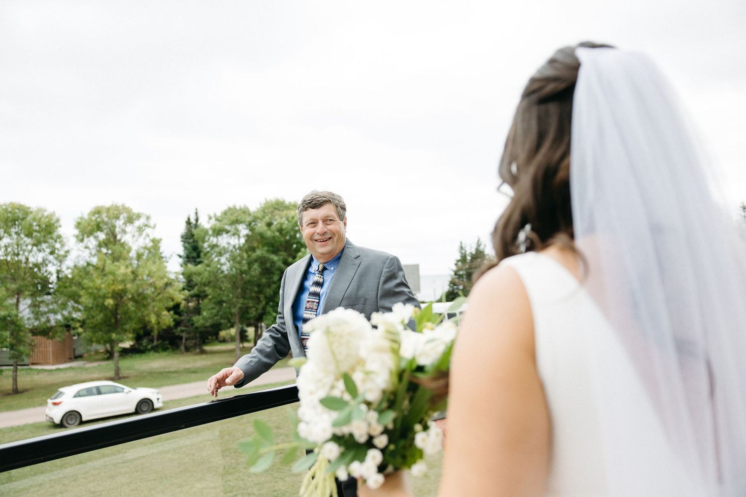 Wedding party members pose with white floral bouquets against an outdoor landscape.