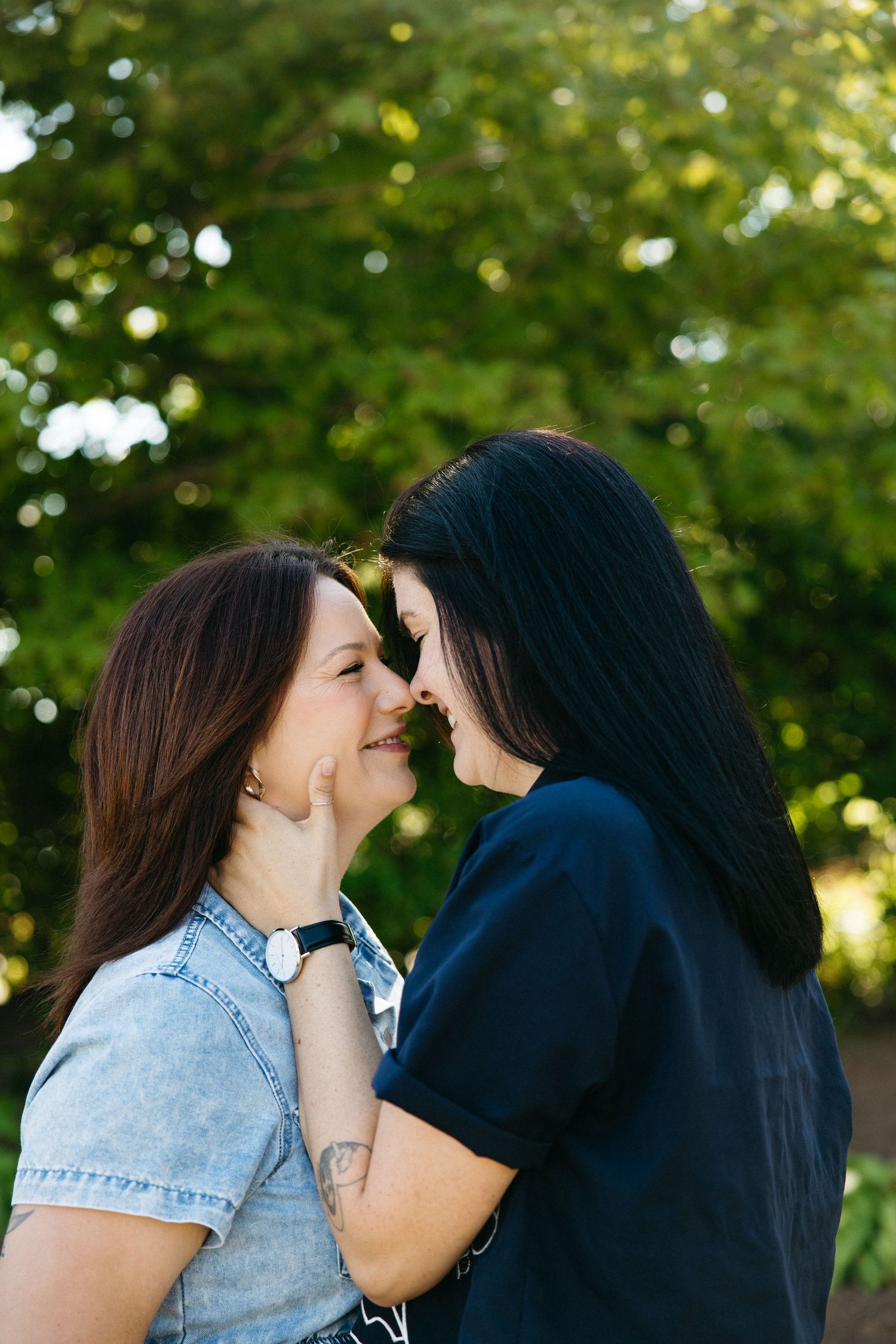 Two people sharing an intimate moment outdoors with green trees in the background.