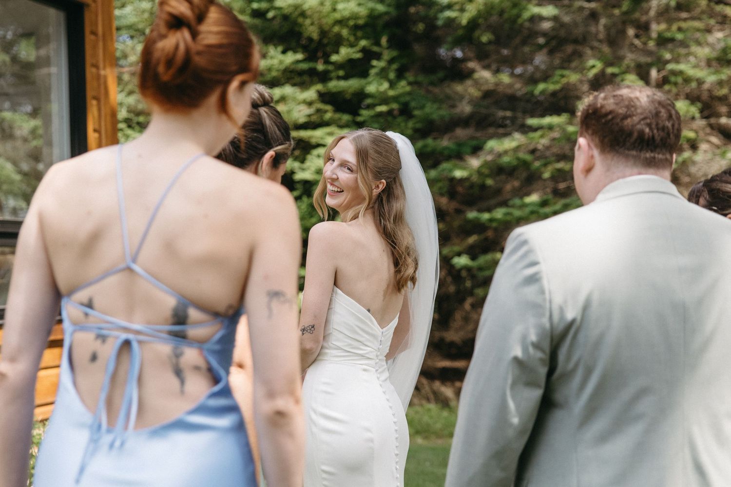 Smiling bride in fitted white gown and veil walks with bridesmaids and groomsmen outdoors at wedding.