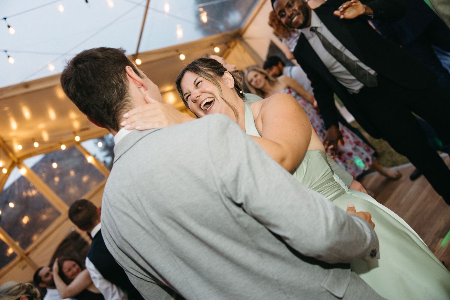 Bride laughing joyfully while dancing with guest at wedding reception.