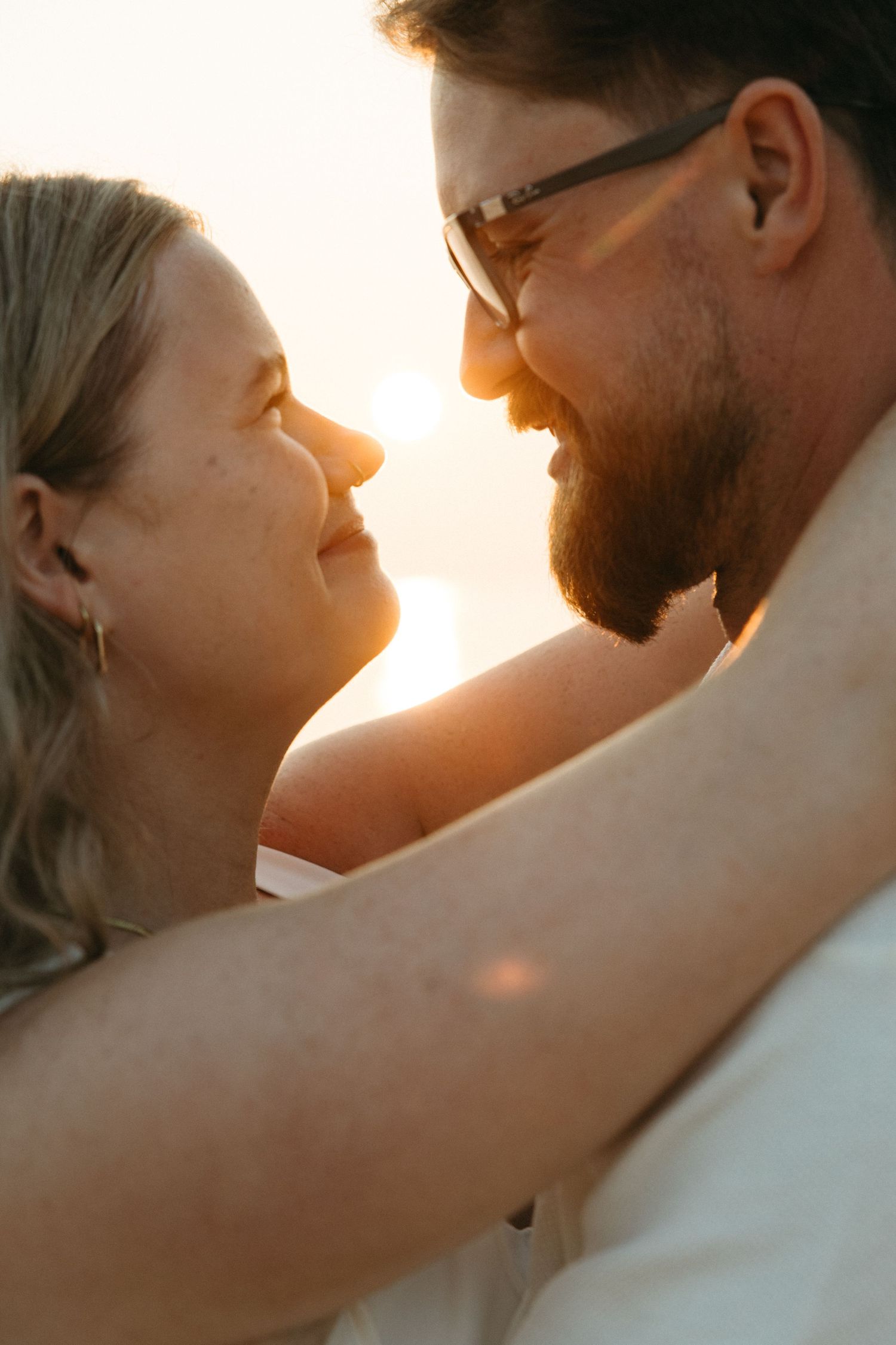 Happy couple sharing a romantic moment at sunset, man with beard and glasses, woman smiling joyfully.