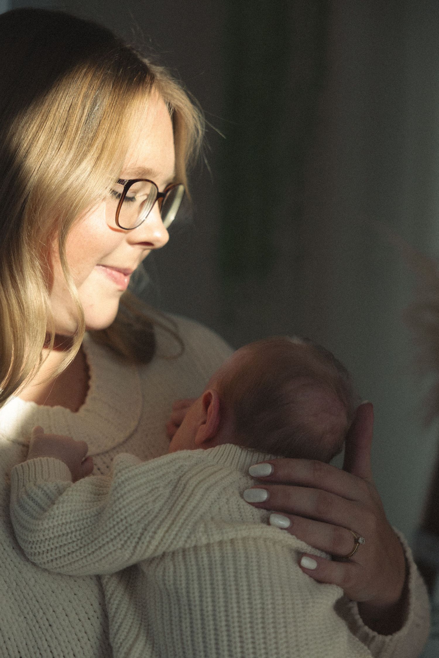 A tender moment showing a person in a cream sweater cradling and gazing at a newborn baby.