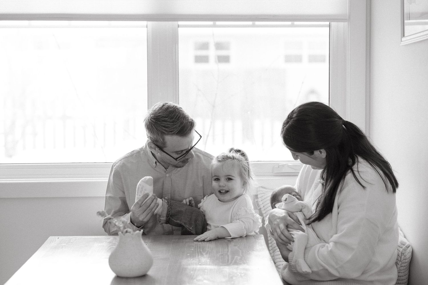 A family sits at a white table enjoying a meal together in a bright sunlit room.