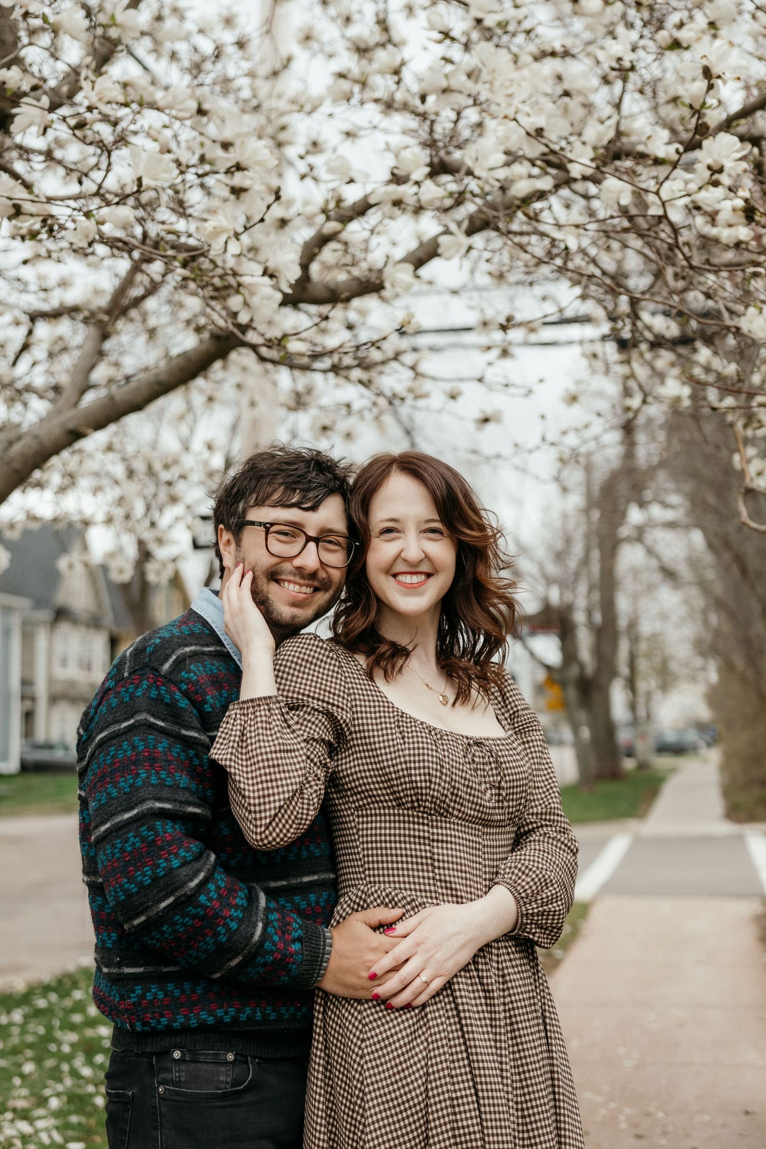 Happy couple embracing under blooming white cherry blossom tree on a sidewalk in spring.