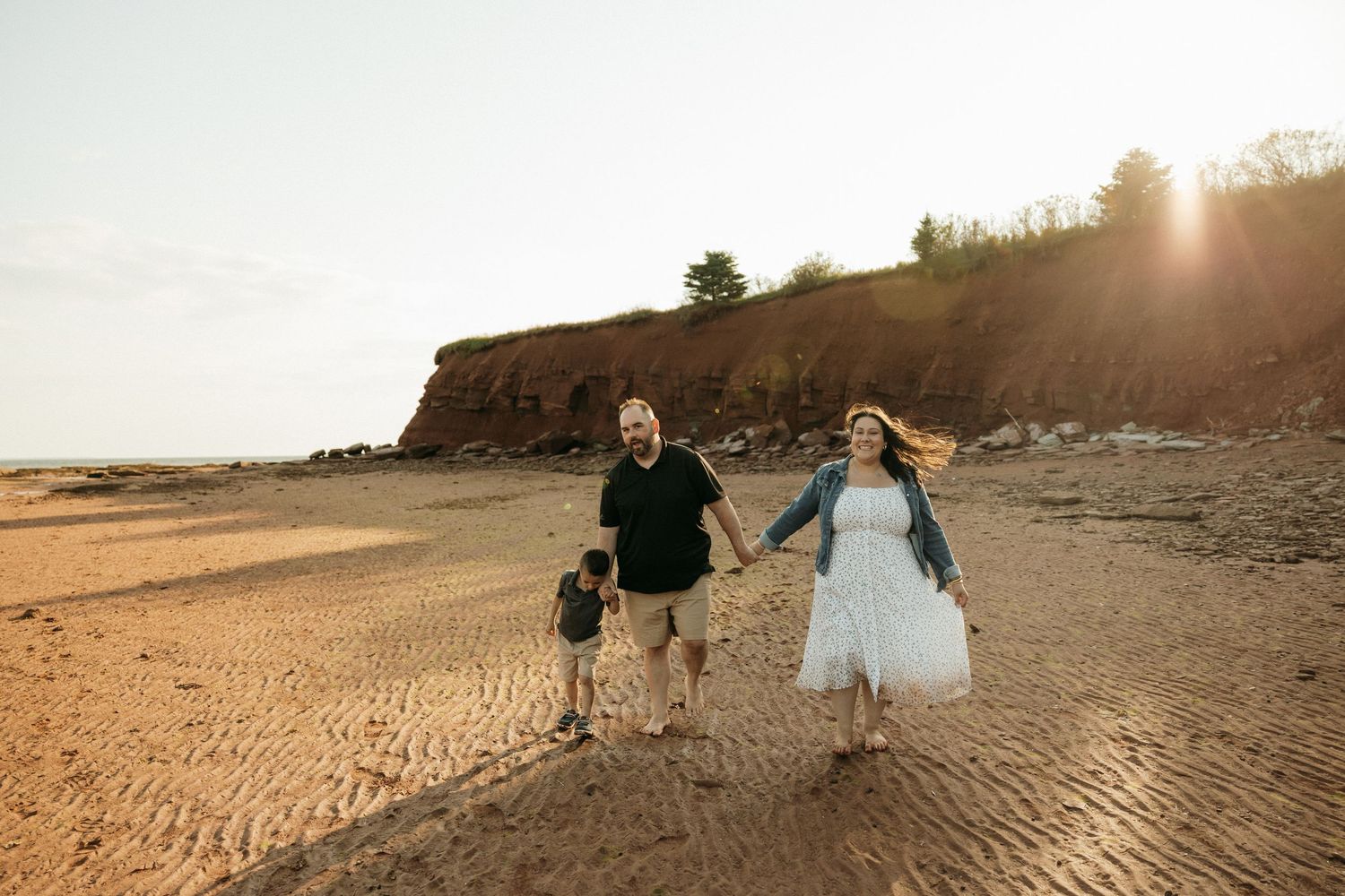 Newlyweds running hand in hand along a scenic beach with cliffs at sunset.