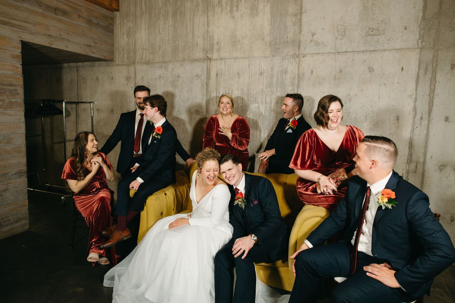 Wedding party members share candid laughs while lounging on yellow couch.