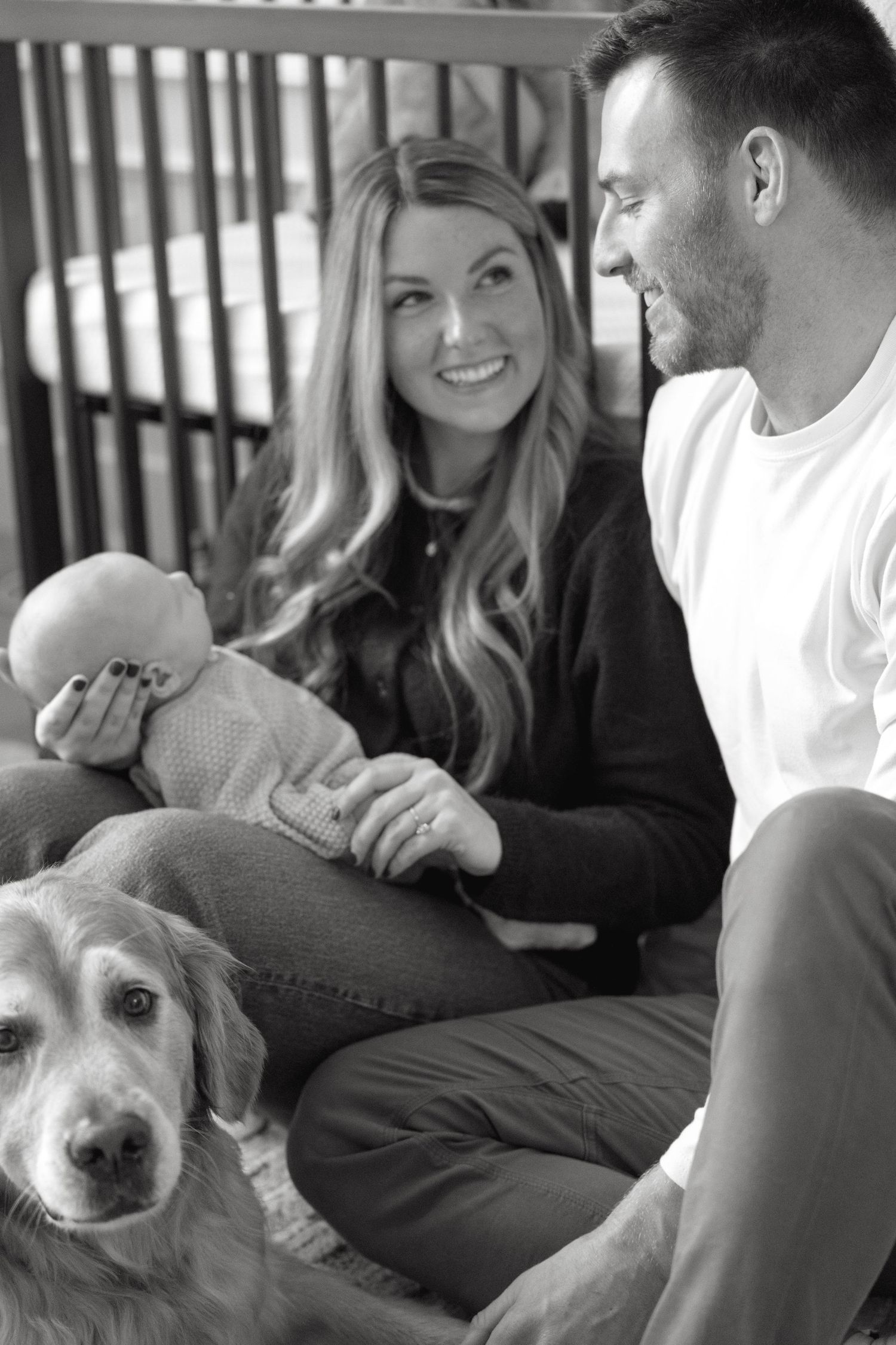 Family gathering on couch with golden retriever and baby in casual setting.
