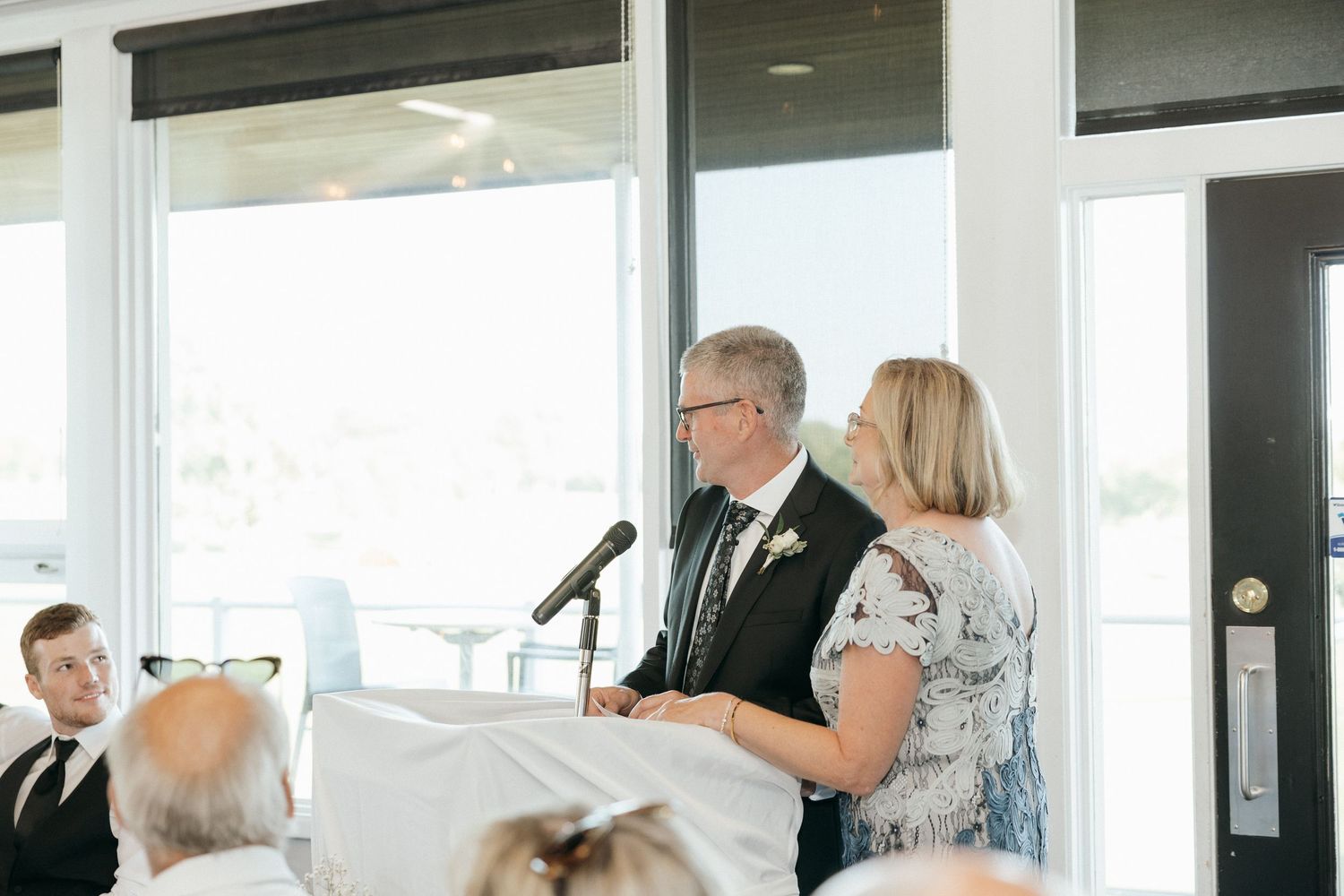 Wedding guests gather in a bright modern venue with floor-to-ceiling windows.