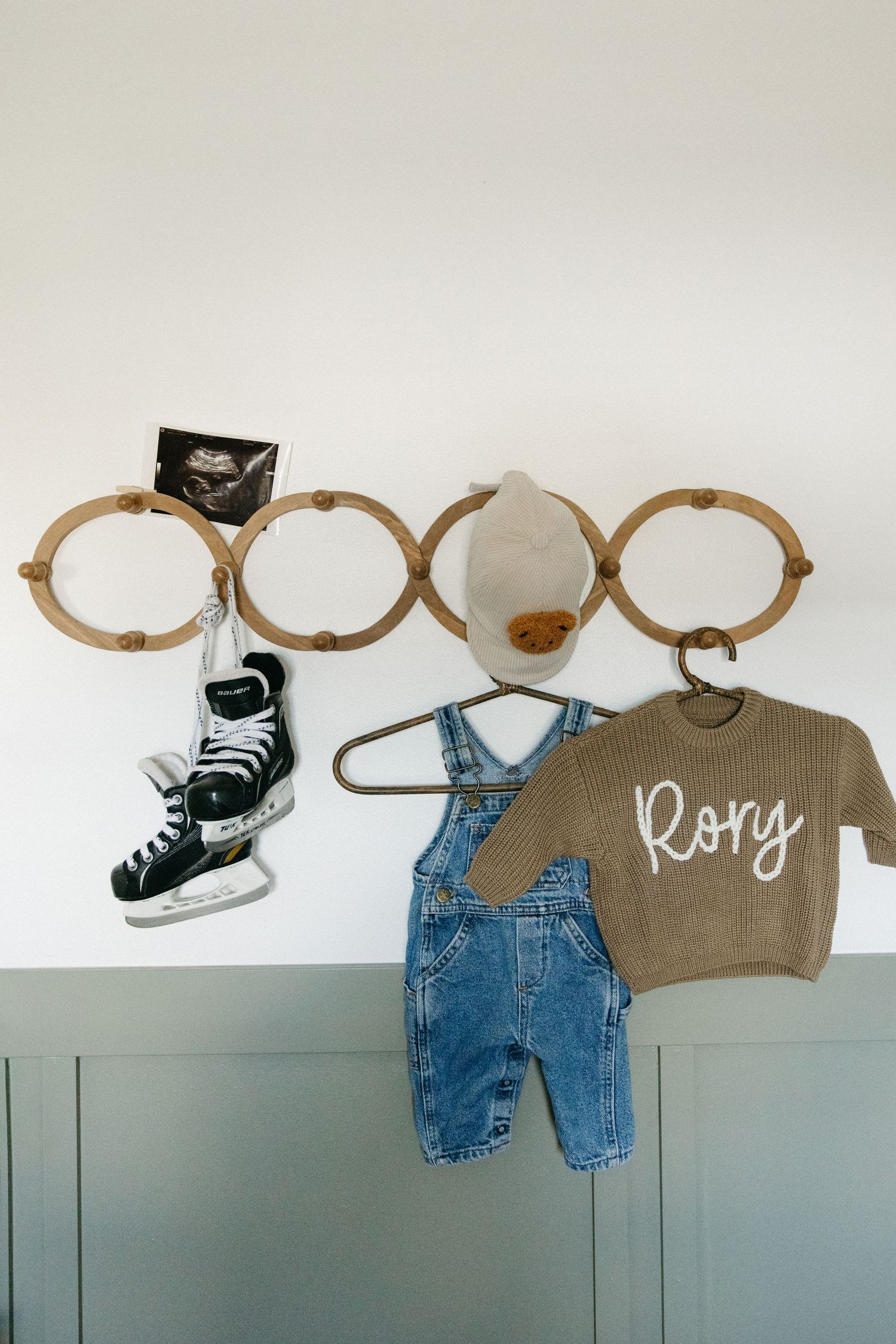 Curved wooden wall hooks holding baby clothes, ice skates, and a knit sweater in a nursery.