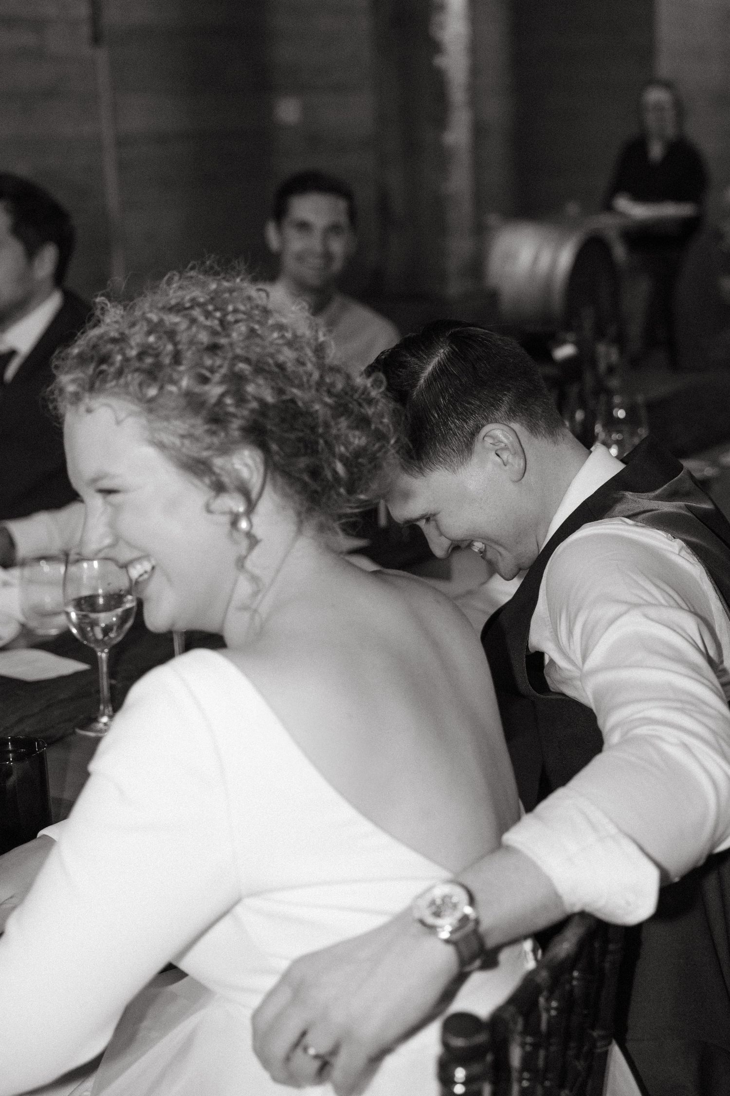 Black and white photo of wedding reception guests laughing together at tables.