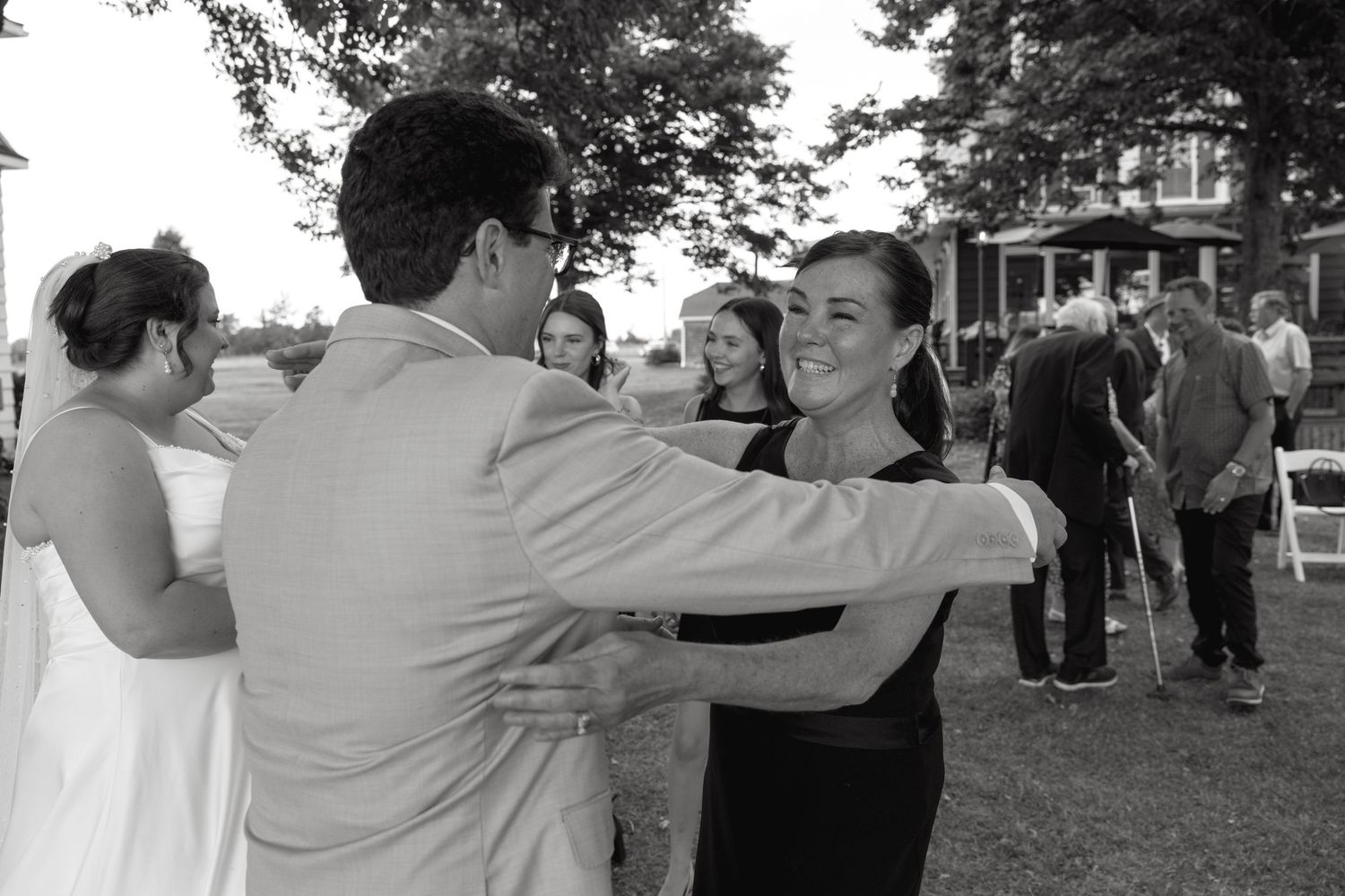 Black and white photo of wedding guests sharing a warm dance and embrace at an outdoor reception.