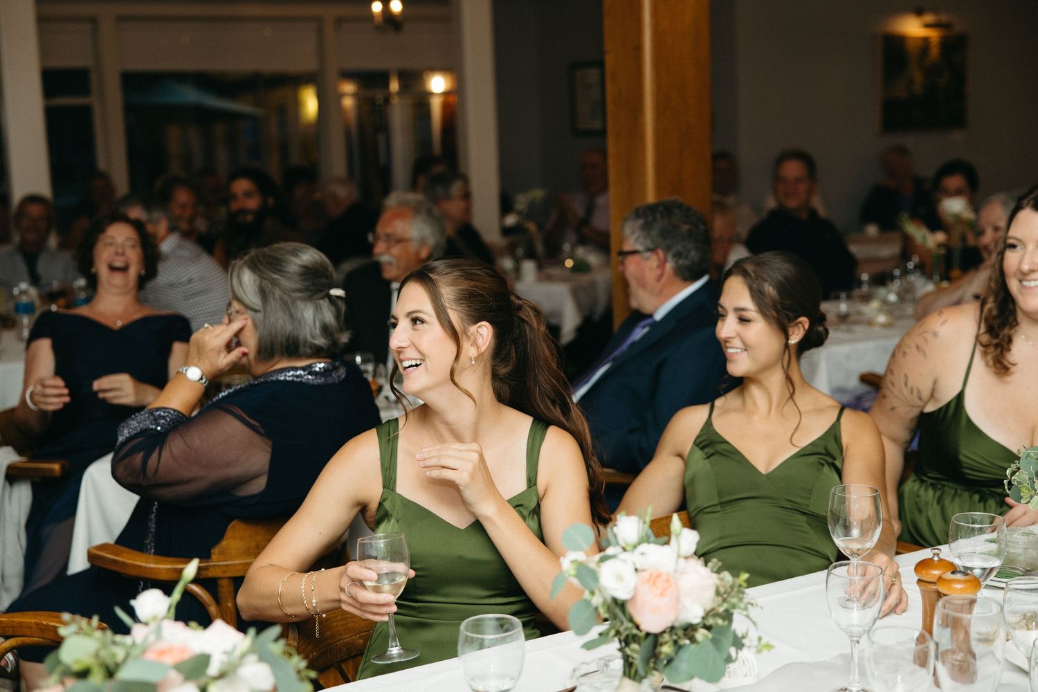 Bridesmaids in green dresses laughing and enjoying wedding reception at elegantly decorated venue.