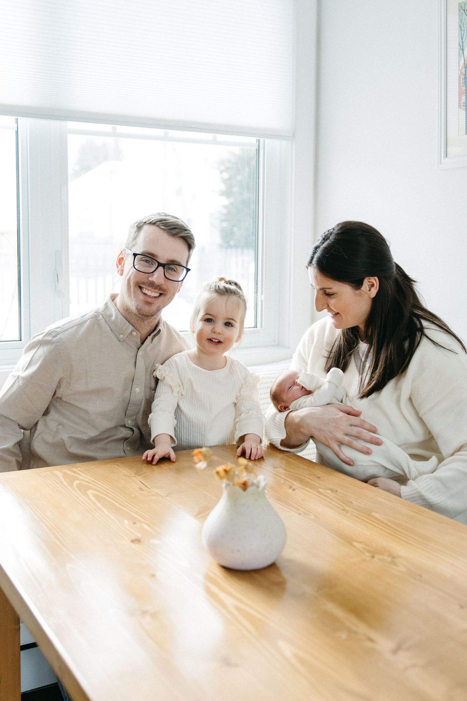 A family gathers around a wooden table sharing a playful moment in a bright white room.
