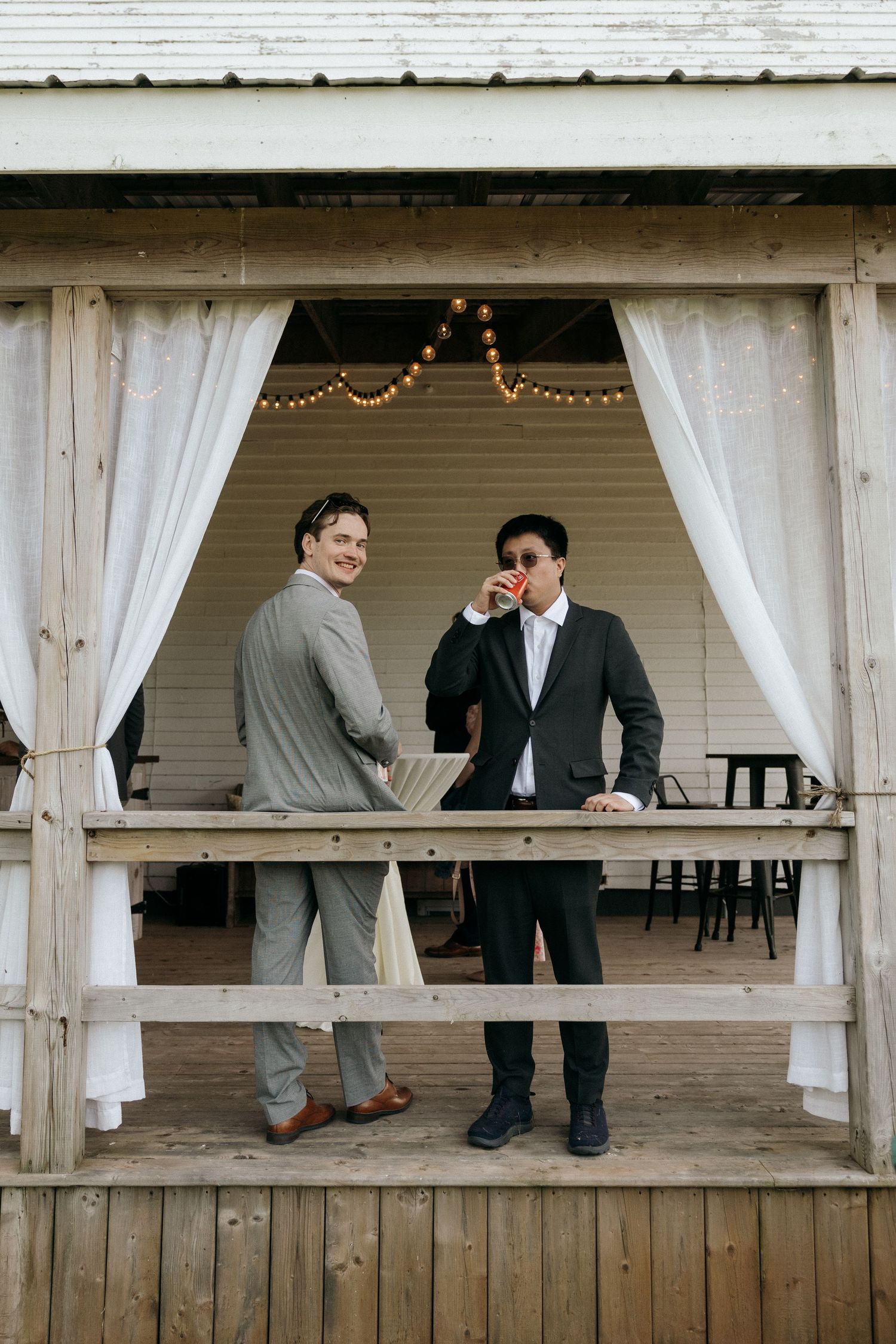 Two guests share a moment under string lights in a rustic wooden pavilion.