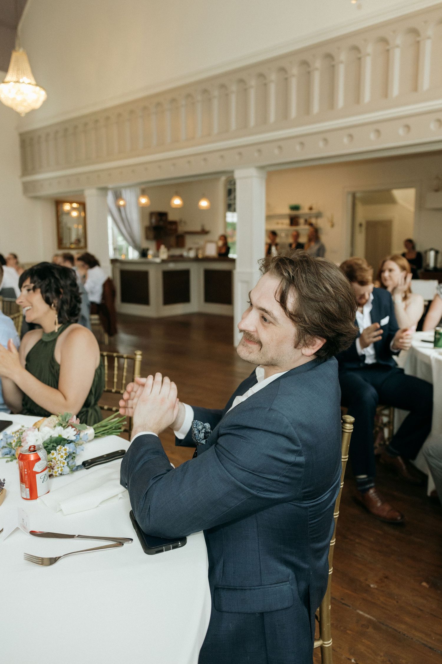 Wedding guests react with laughter and emotion during reception speeches in an elegant ballroom.