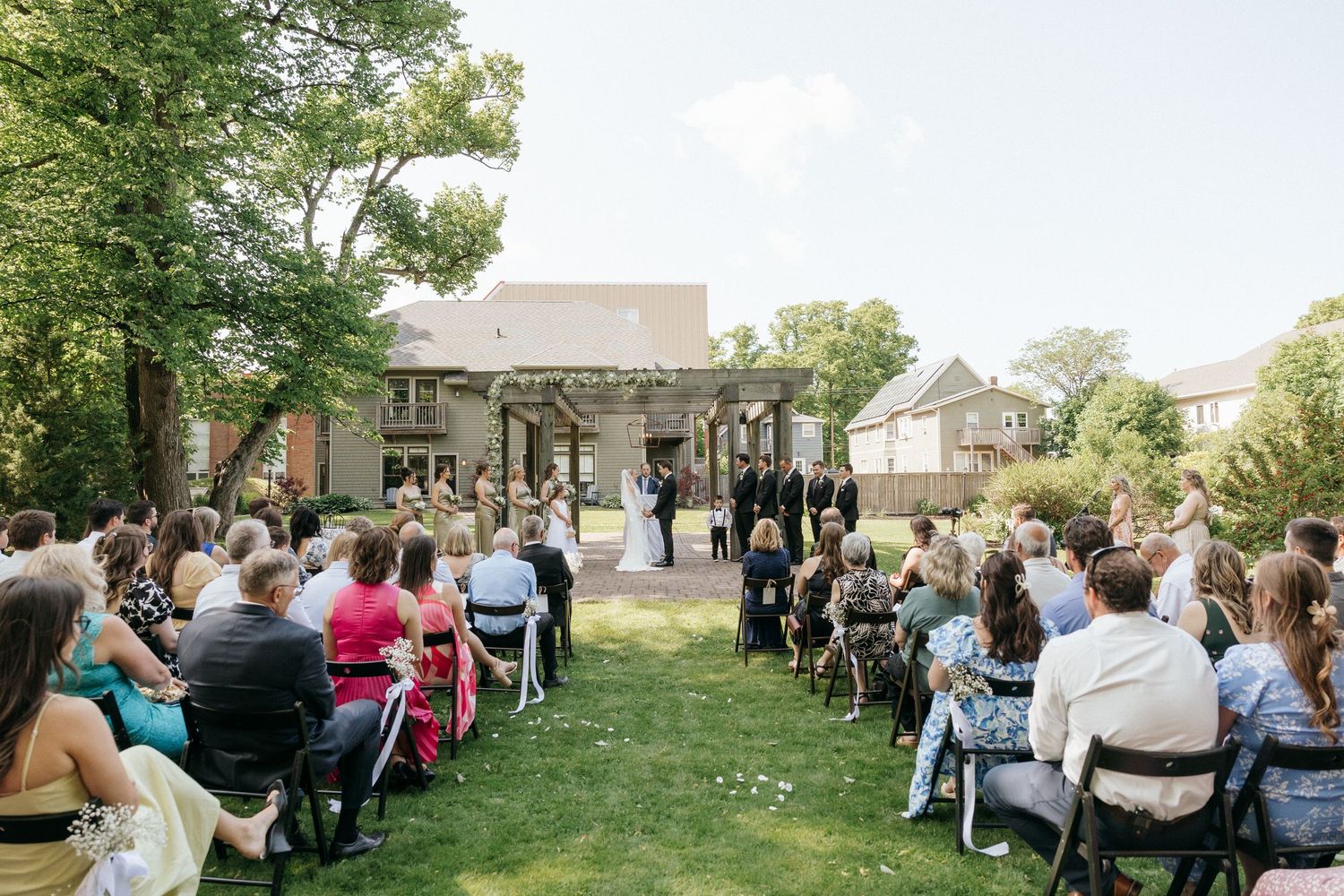 Wide view of outdoor wedding ceremony with guests seated on white chairs.